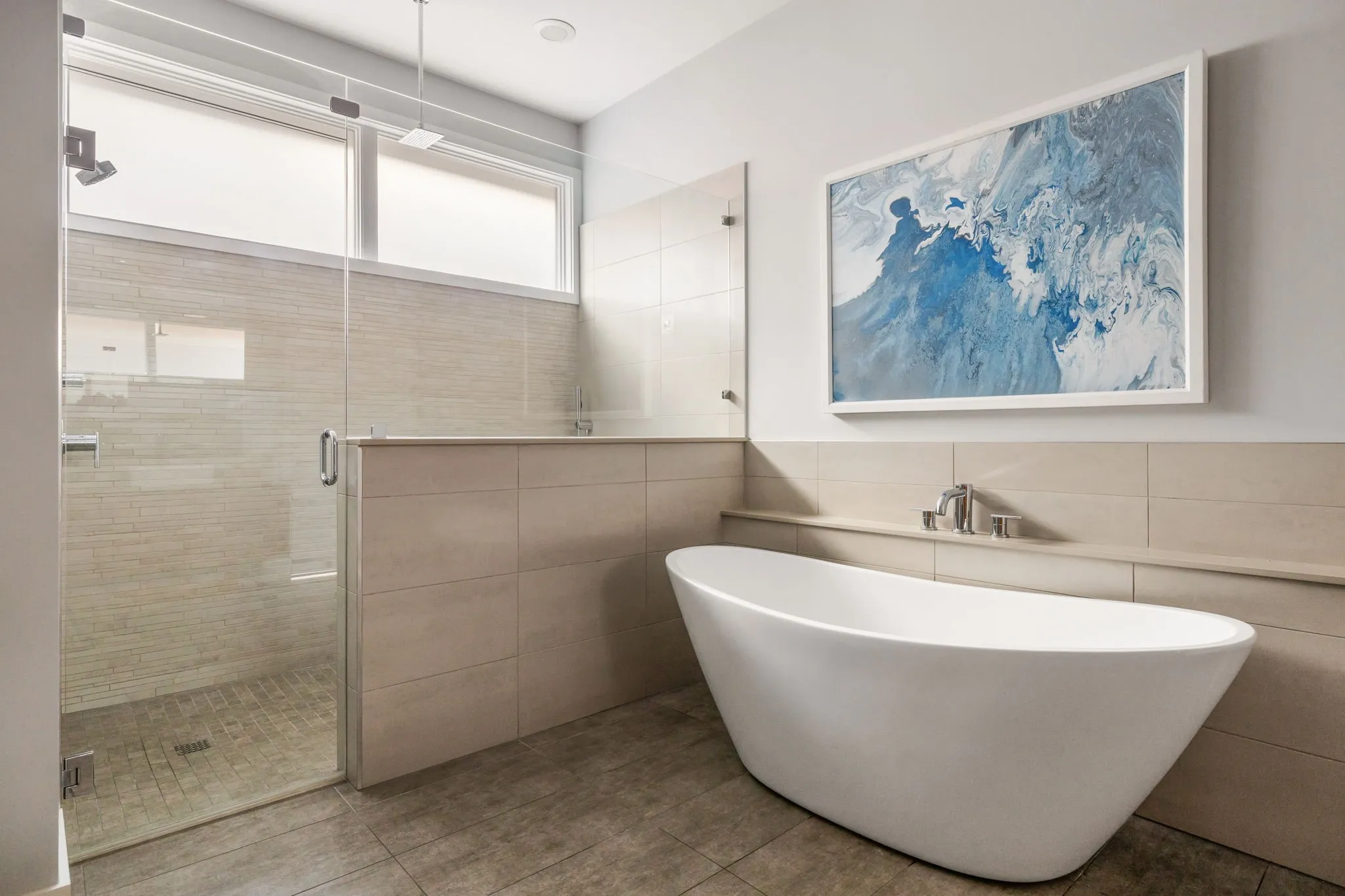 Freestanding soaking tub, glass-enclosed shower, tiled half-wall, and transom windows