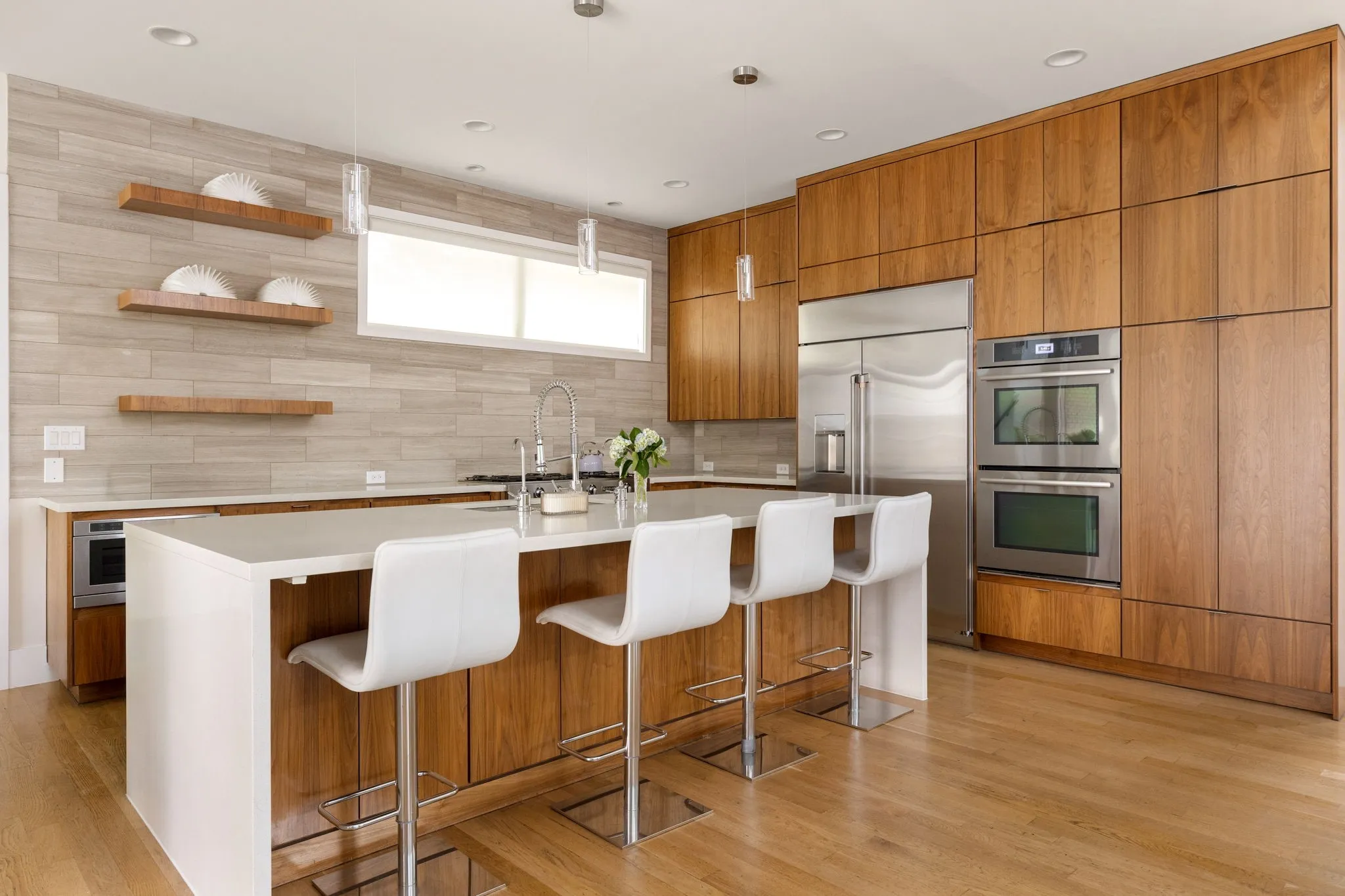 Gourmet kitchen with wood-finish flooring, full-height wood cabinetry, stainless steel double ovens, stainless steel refrigerator, and an expansive island with a waterfall countertop