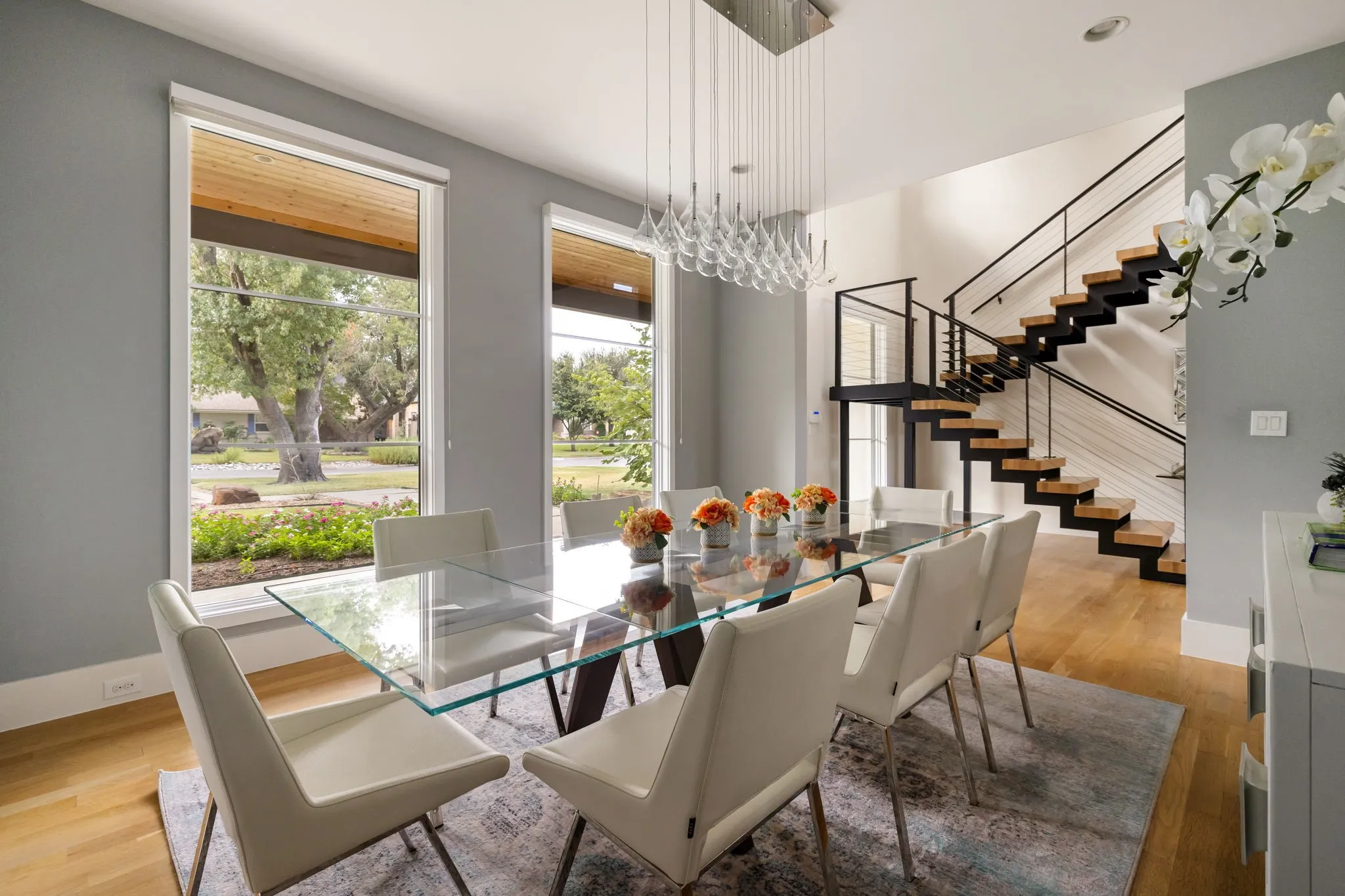 Hardwood flooring, floor-to-ceiling windows, modern floating staircase with black railings, high ceilings, and a contemporary chandelier