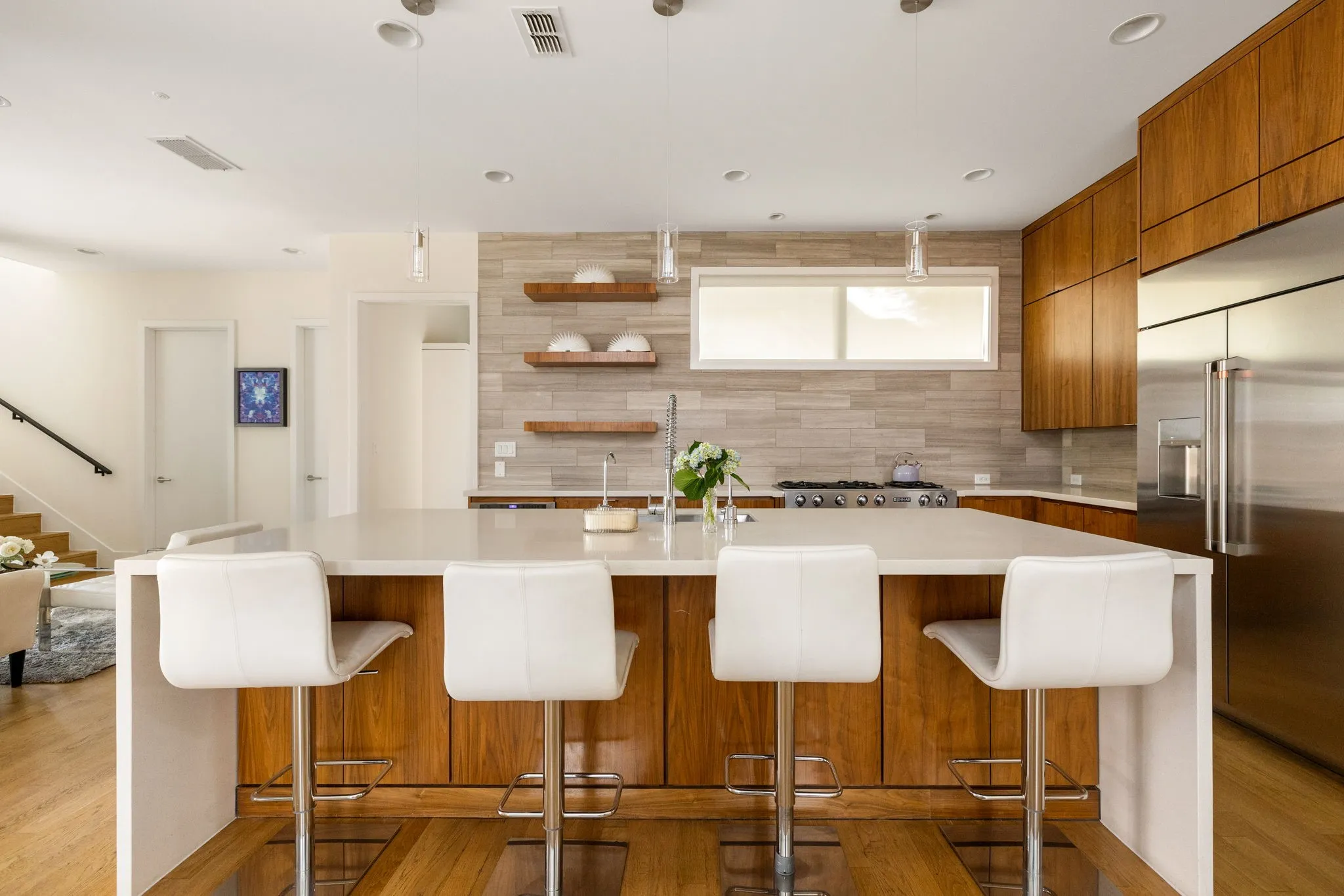 Light wood-finish flooring throughout, high ceilings, large sliding glass doors, recessed lighting, and a kitchen island with bar seating