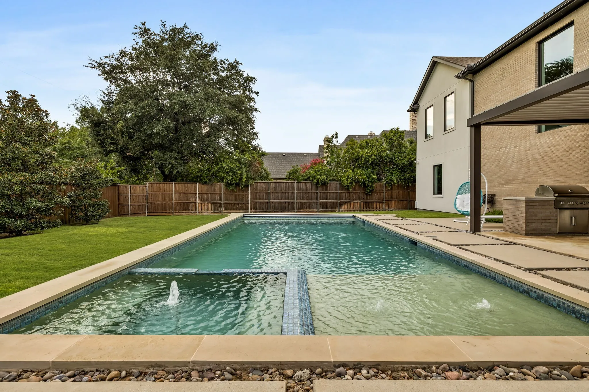 Expansive backyard featuring a rectangular swimming pool with integrated water features, stone coping, and a surrounding patio