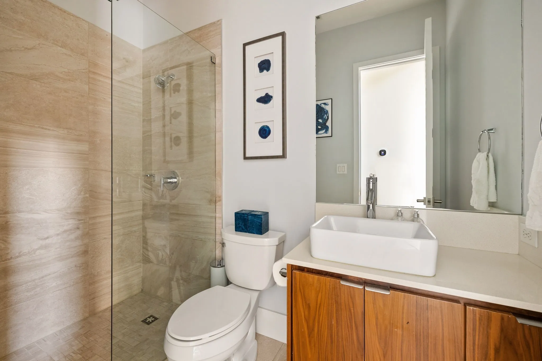 Glass-enclosed shower with natural-toned tile surround, chrome fixtures, wood-finish vanity, white vessel sink, and an integrated countertop