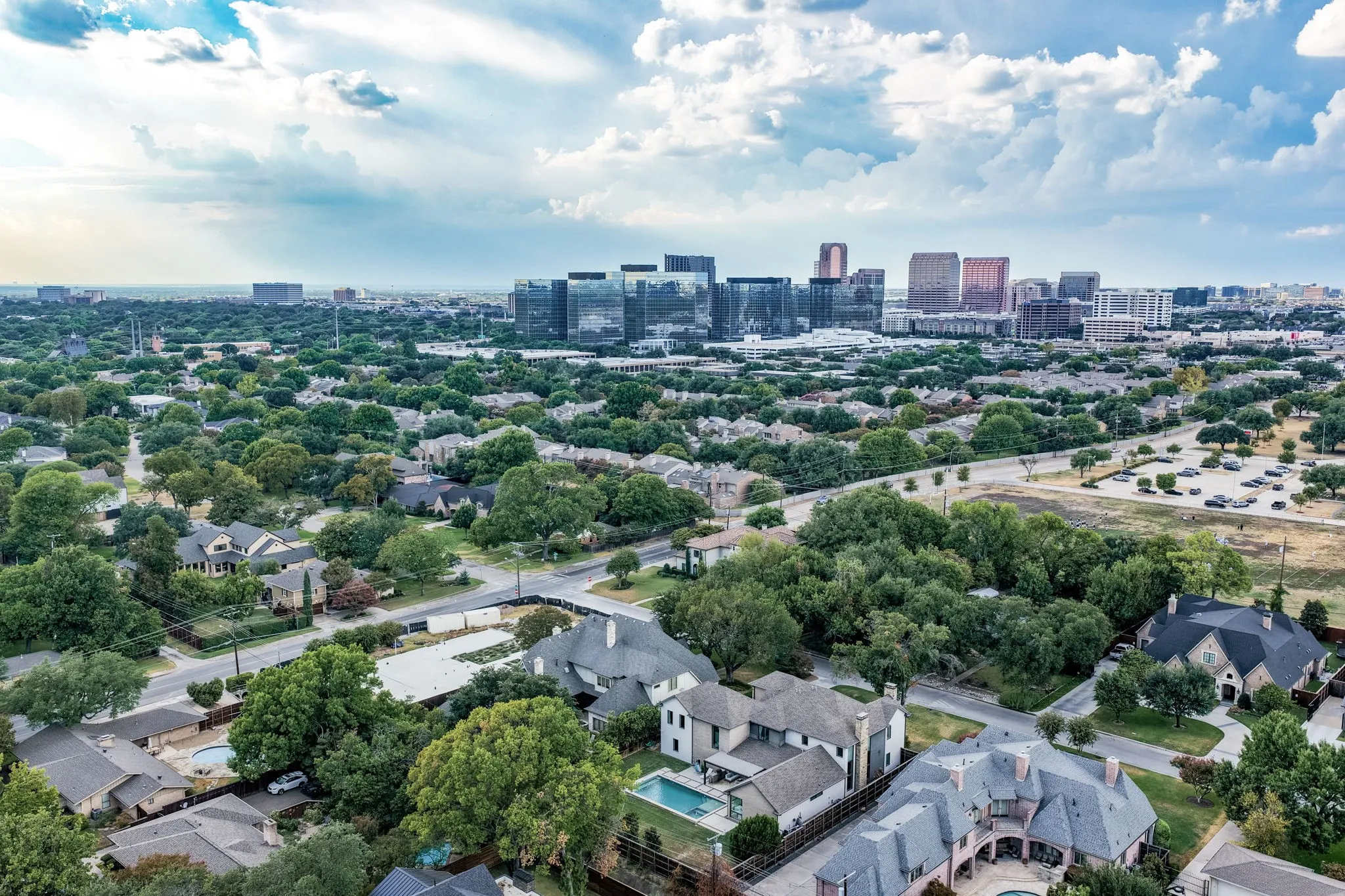 Aerial perspective featuring residential properties, mature tree canopy, and distant city skyline