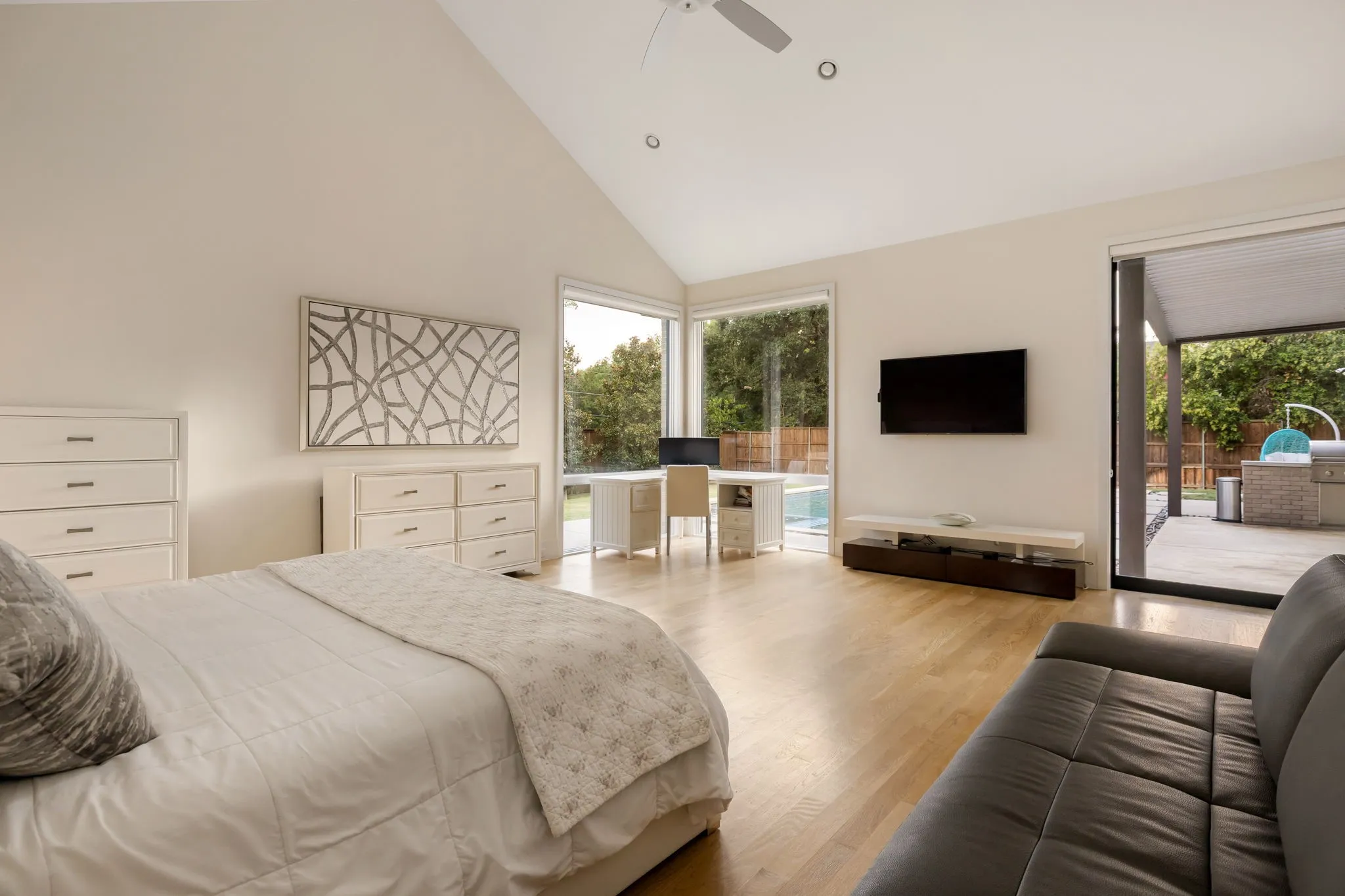 Vaulted ceiling with recessed lighting, wood-finish flooring, corner window, sliding glass door, and an outdoor patio with a built-in grill