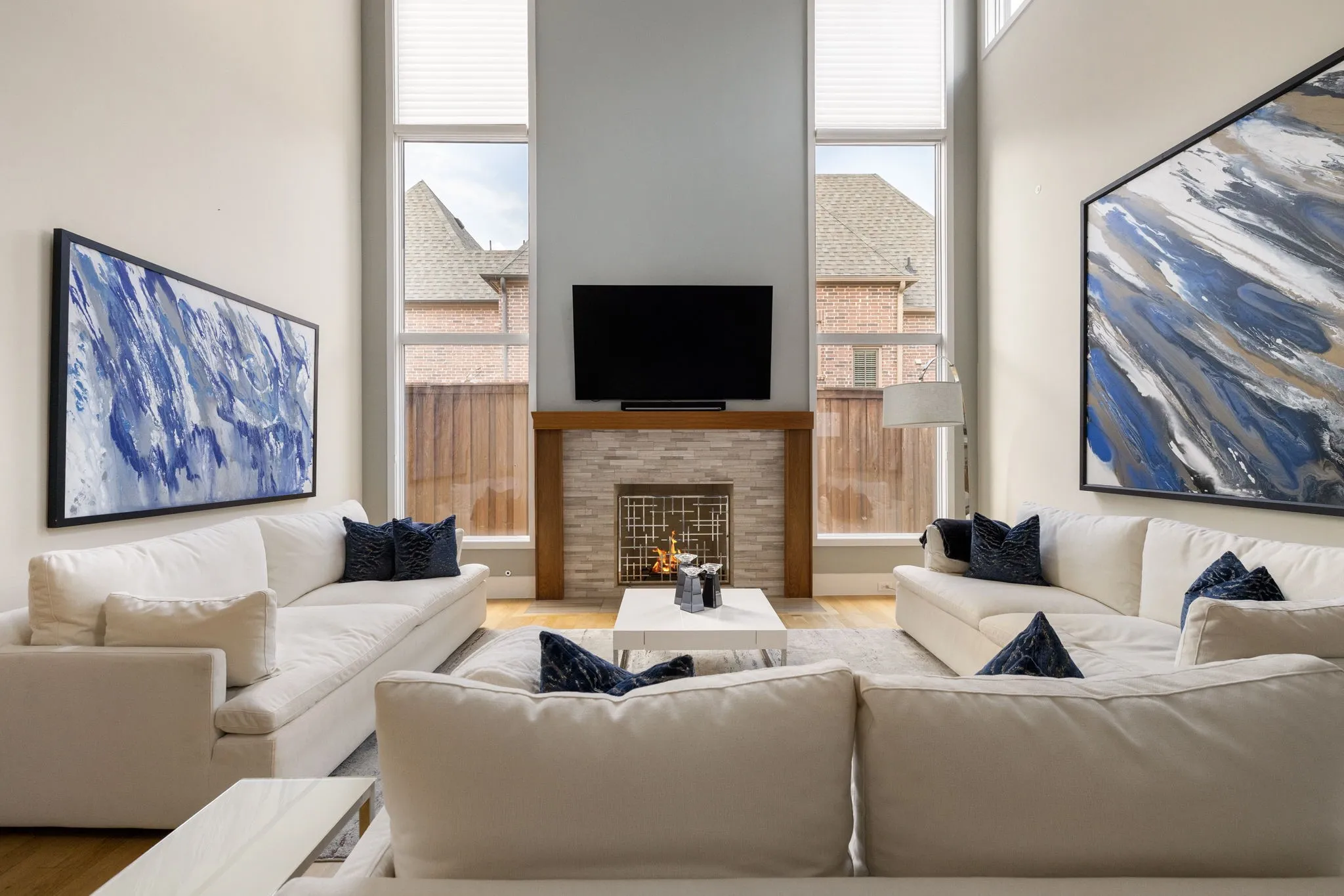Vaulted ceilings, stone-clad fireplace with wood mantel, tall windows, wood-finish flooring, and light wall tones