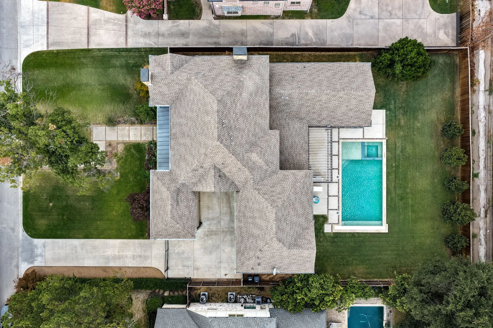 Expansive property featuring a multi-gabled roofline, concrete driveway, and a large inground swimming pool with an integrated spa