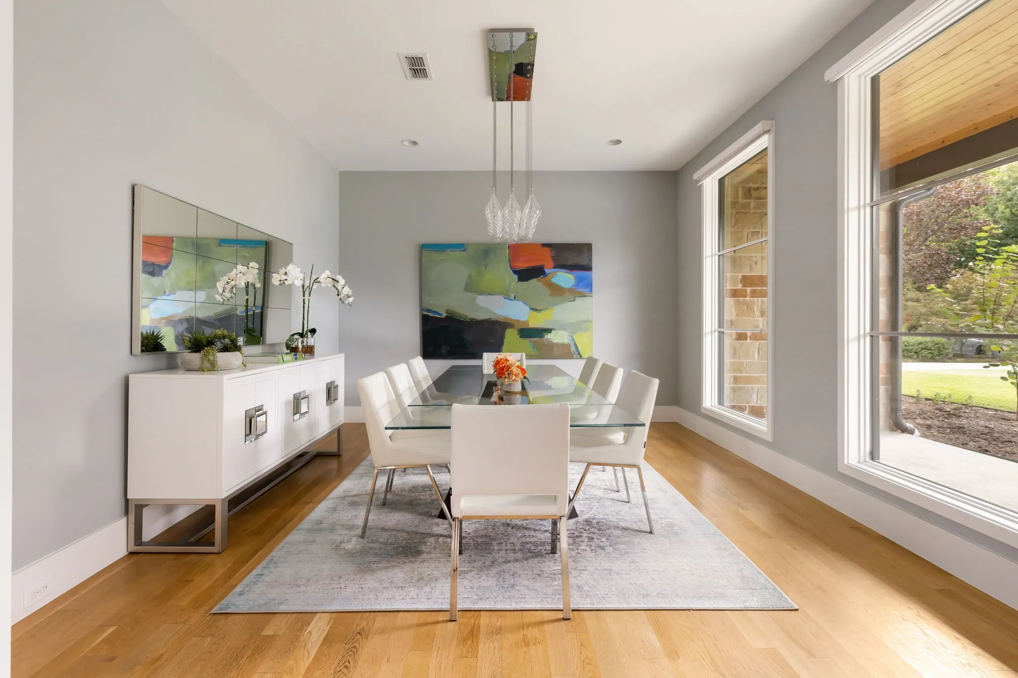 Bright dining area showcasing hardwood flooring, a white pendant light fixture, and expansive windows framing natural landscaping