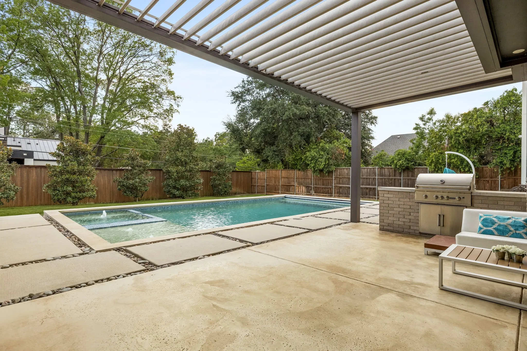 Outdoor living space featuring a louvered pergola, built-in BBQ station, swimming pool with integrated spa, and concrete paver patio