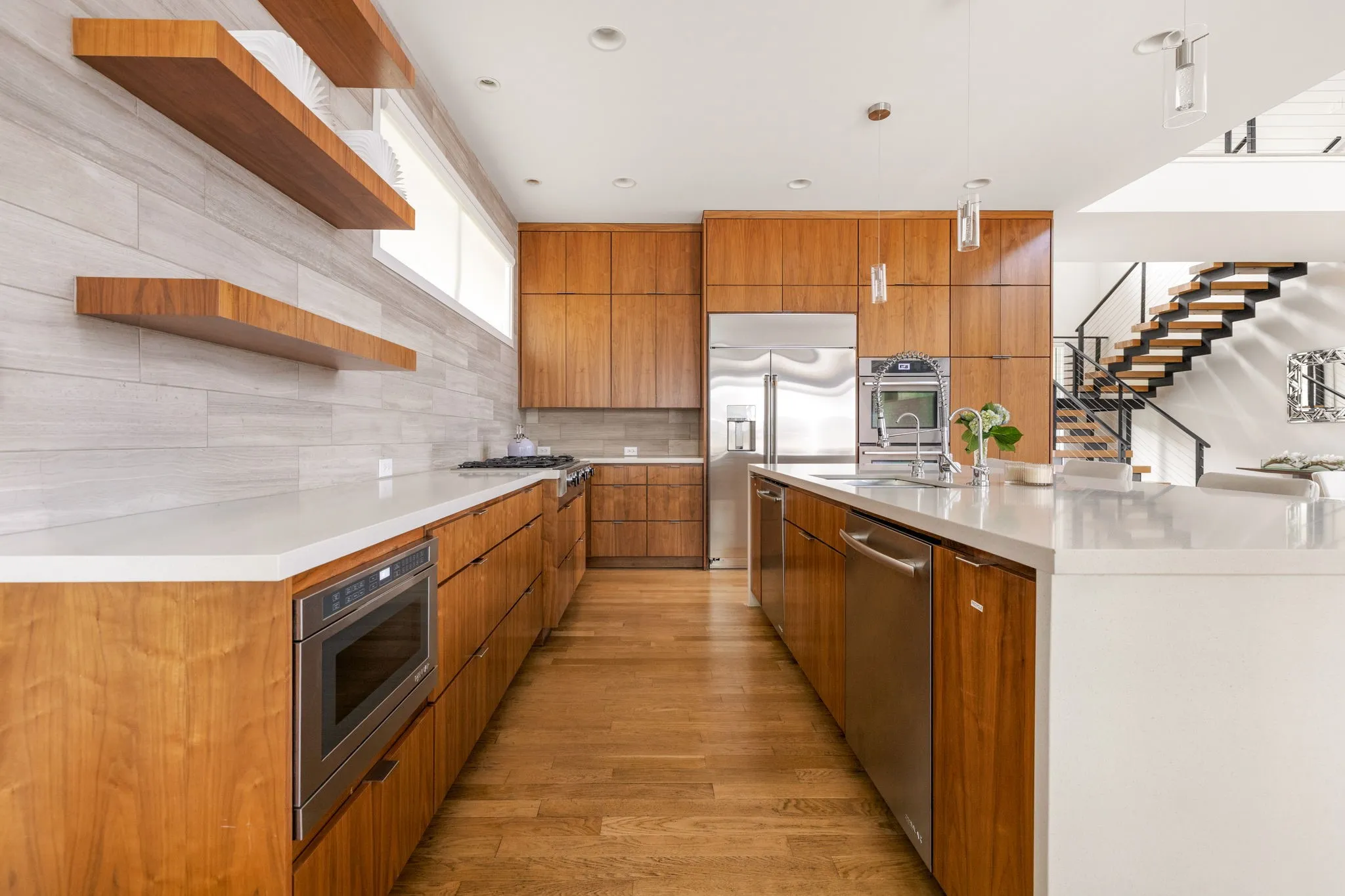 Hardwood flooring throughout, extensive wood cabinetry, stainless steel appliances, white countertops, and a modern open-tread staircase