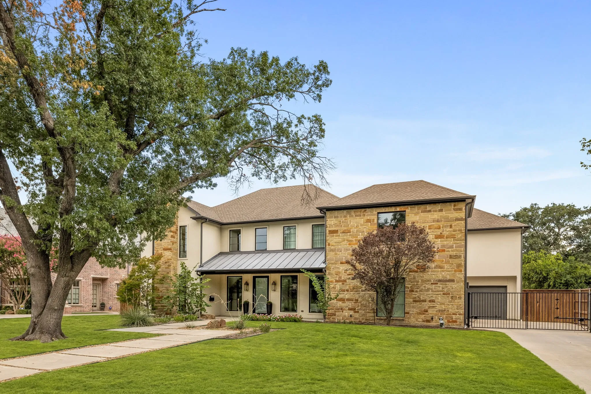 Stucco and stone exterior with a covered entry, dark-framed windows, and a metal roof accent