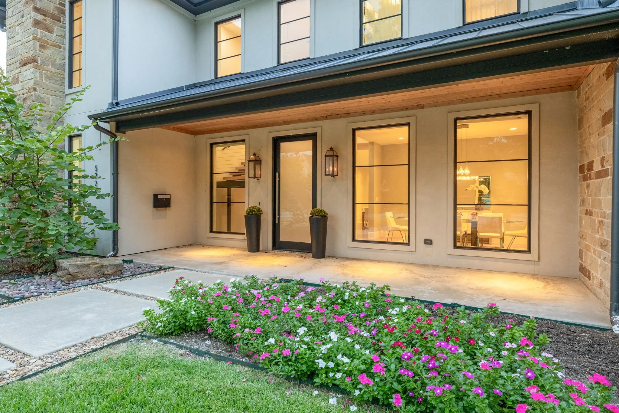 Contemporary exterior with stucco facade, stone accents, black-framed windows, wood-paneled soffit, and concrete walkway
