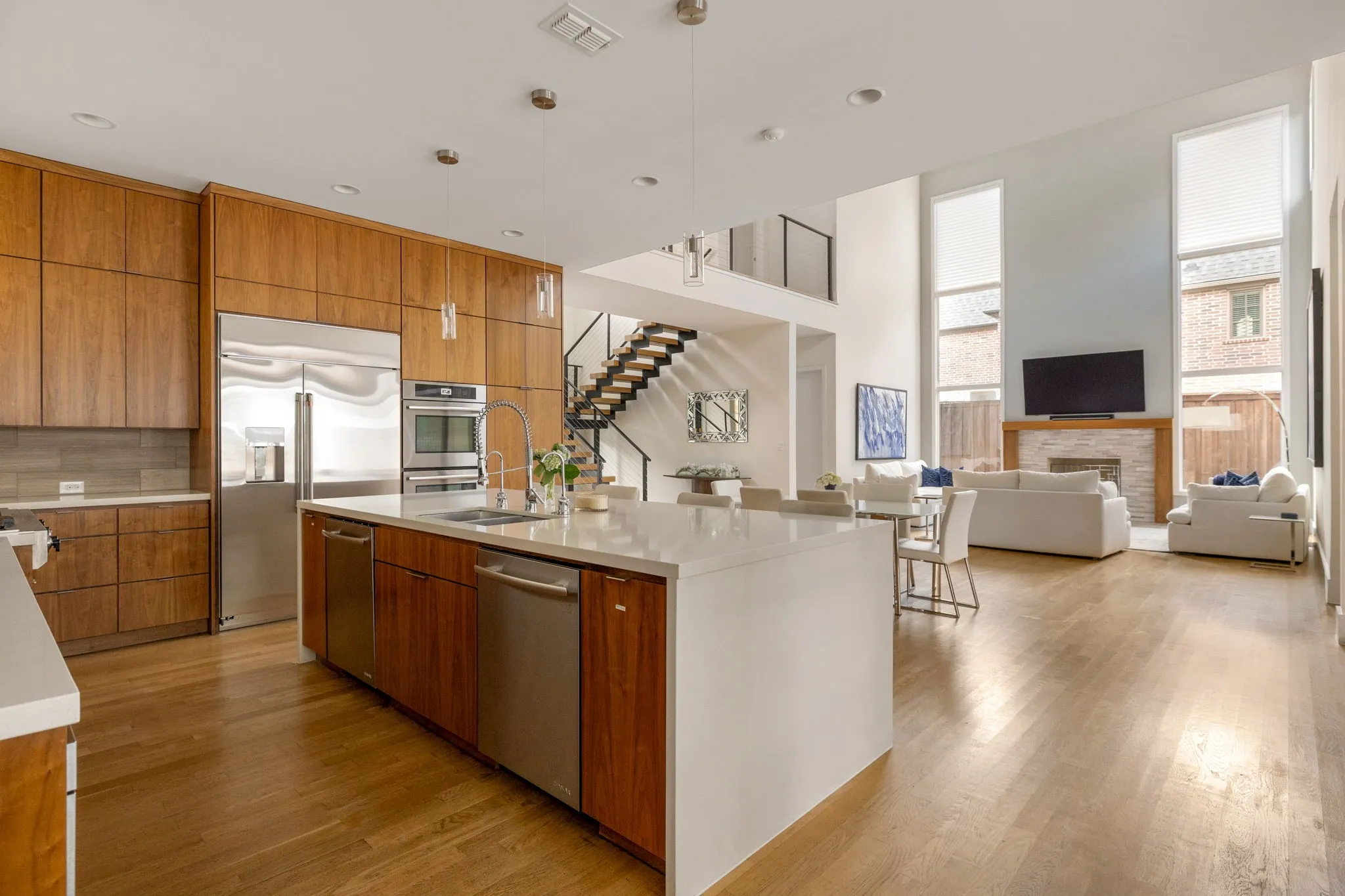 Hardwood flooring throughout, a kitchen featuring wood cabinetry and stainless steel appliances, a large central island with seating, a living area with a stone fireplace, and a two-story ceiling