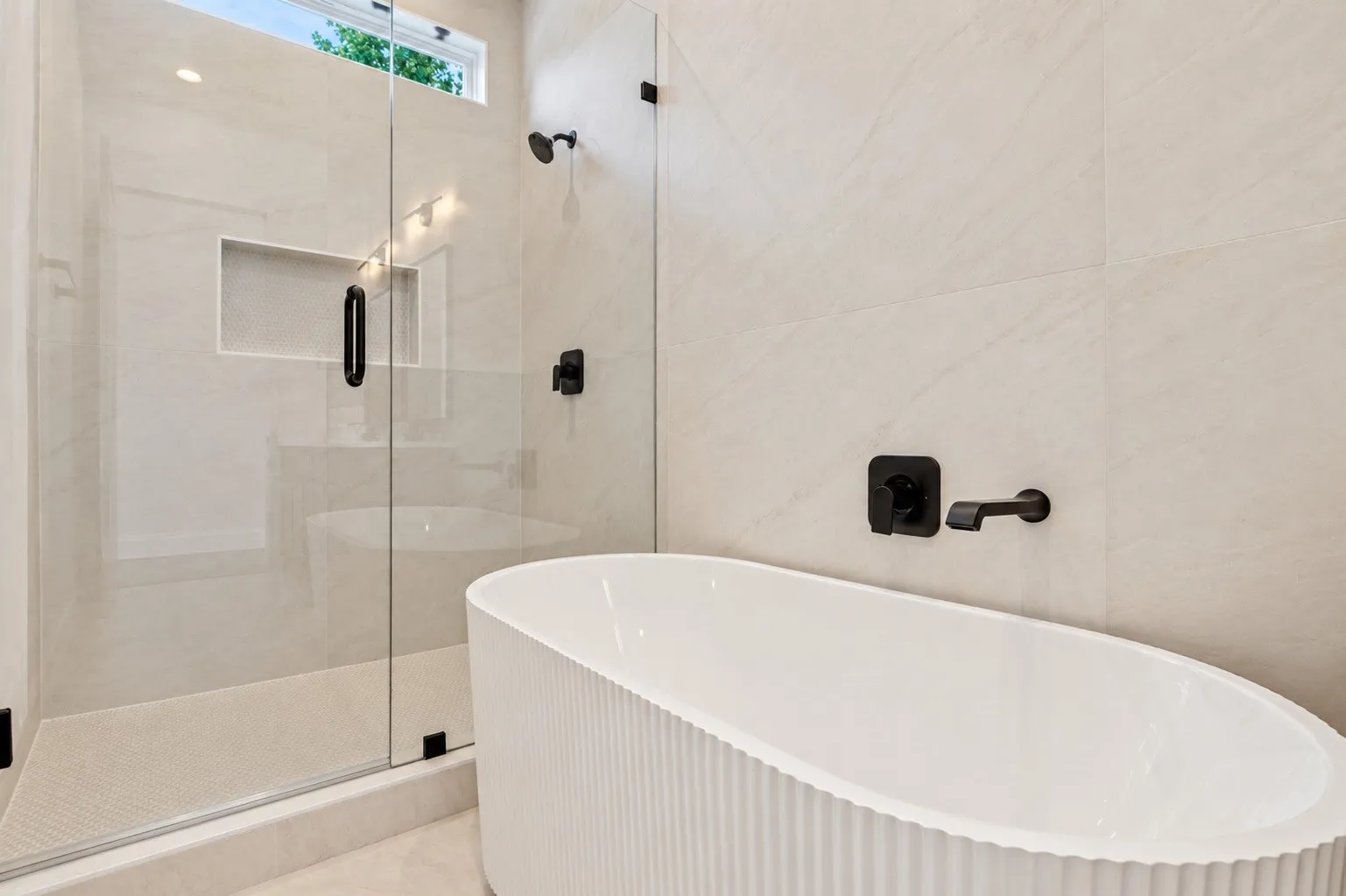 Freestanding soaking tub, glass-enclosed shower with a recessed niche, and matte black fixtures