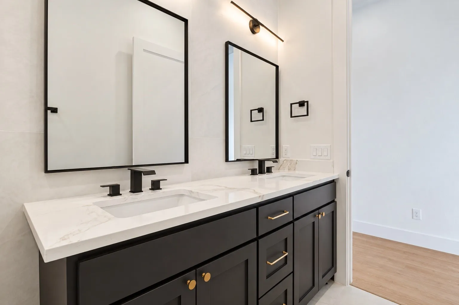 Dual vanity with integrated sinks, white countertop, black cabinetry, and gold-tone hardware