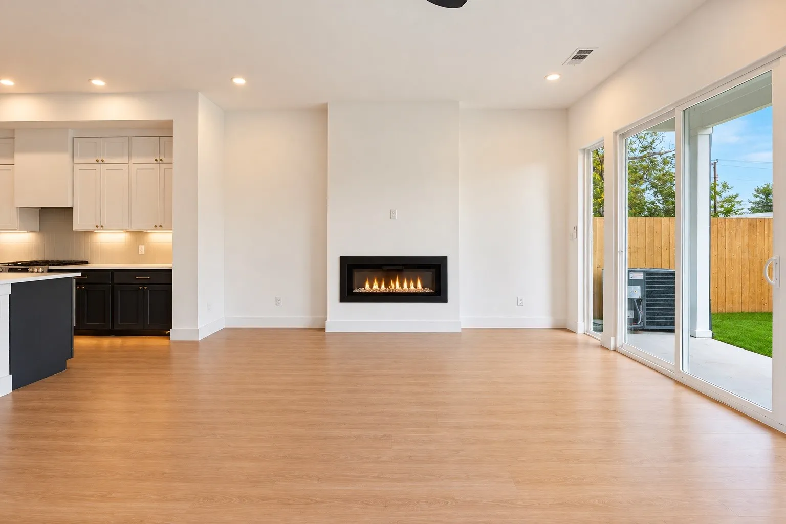Wood-finish flooring, built-in linear fireplace, recessed lighting, and kitchen with light and dark cabinetry
