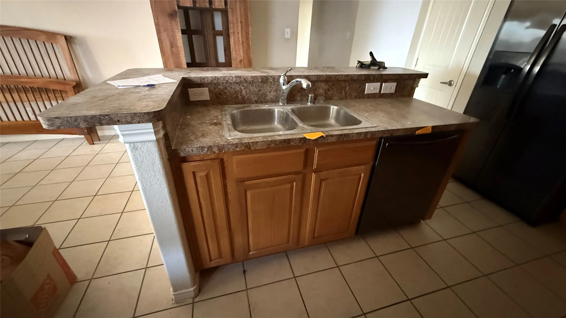 Kitchen island with dual basin stainless steel sink, dark finish countertop, wood-finish cabinetry, and an integrated dishwasher