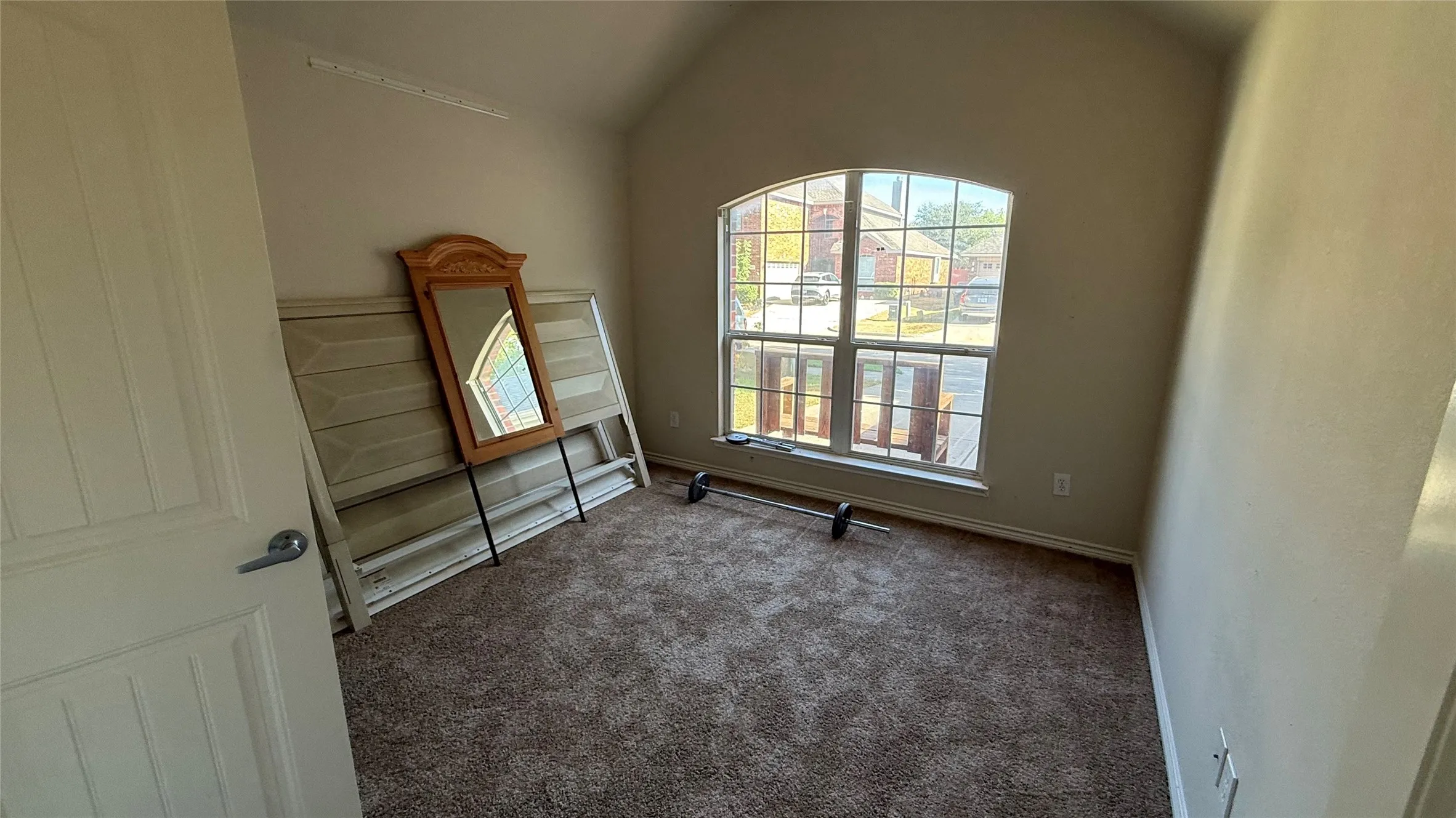Arched window with gridded panes, vaulted ceiling, and neutral-toned carpet flooring