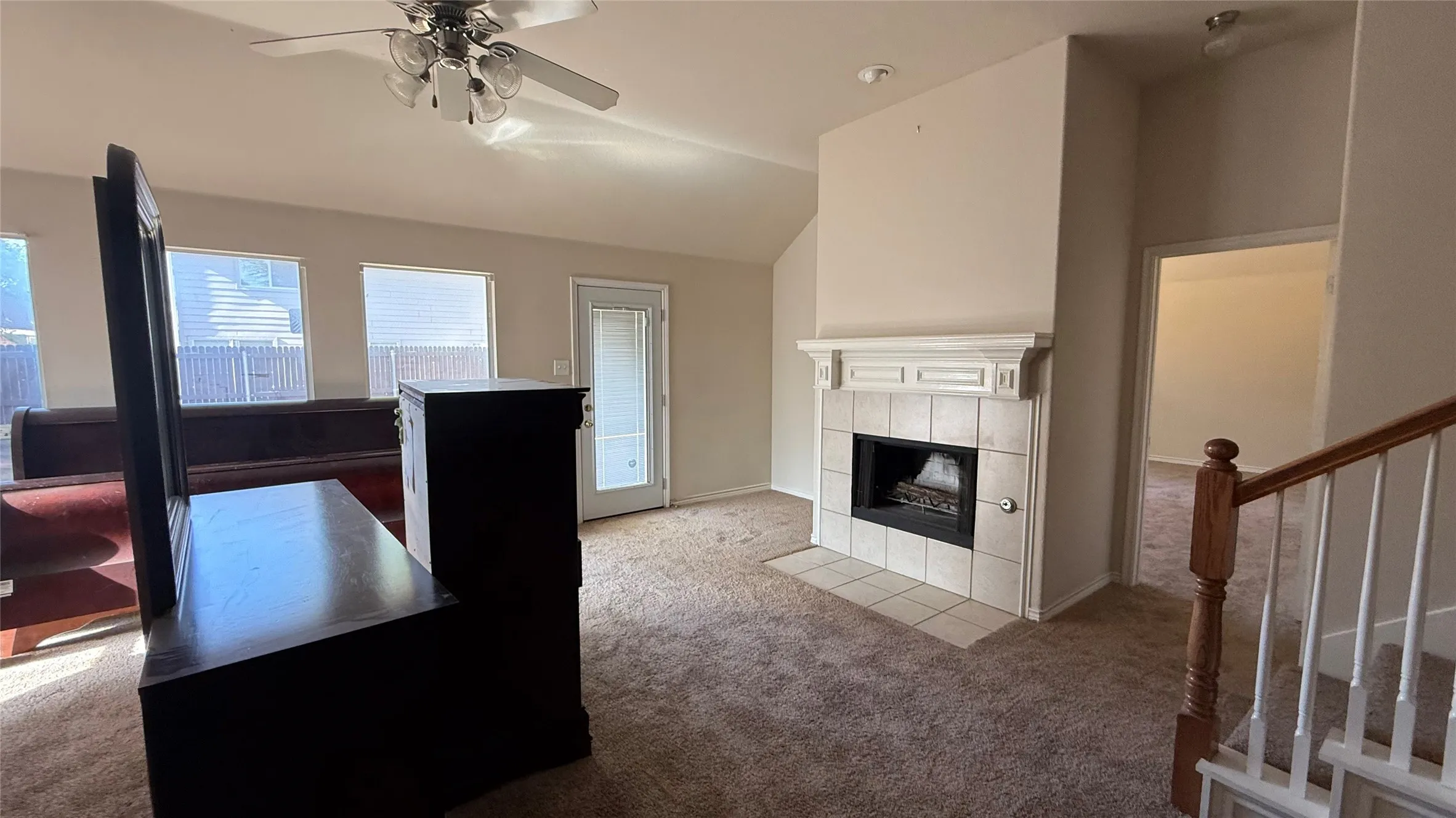 Living area with vaulted ceilings, a fireplace with a tile surround and mantel, and a ceiling fan