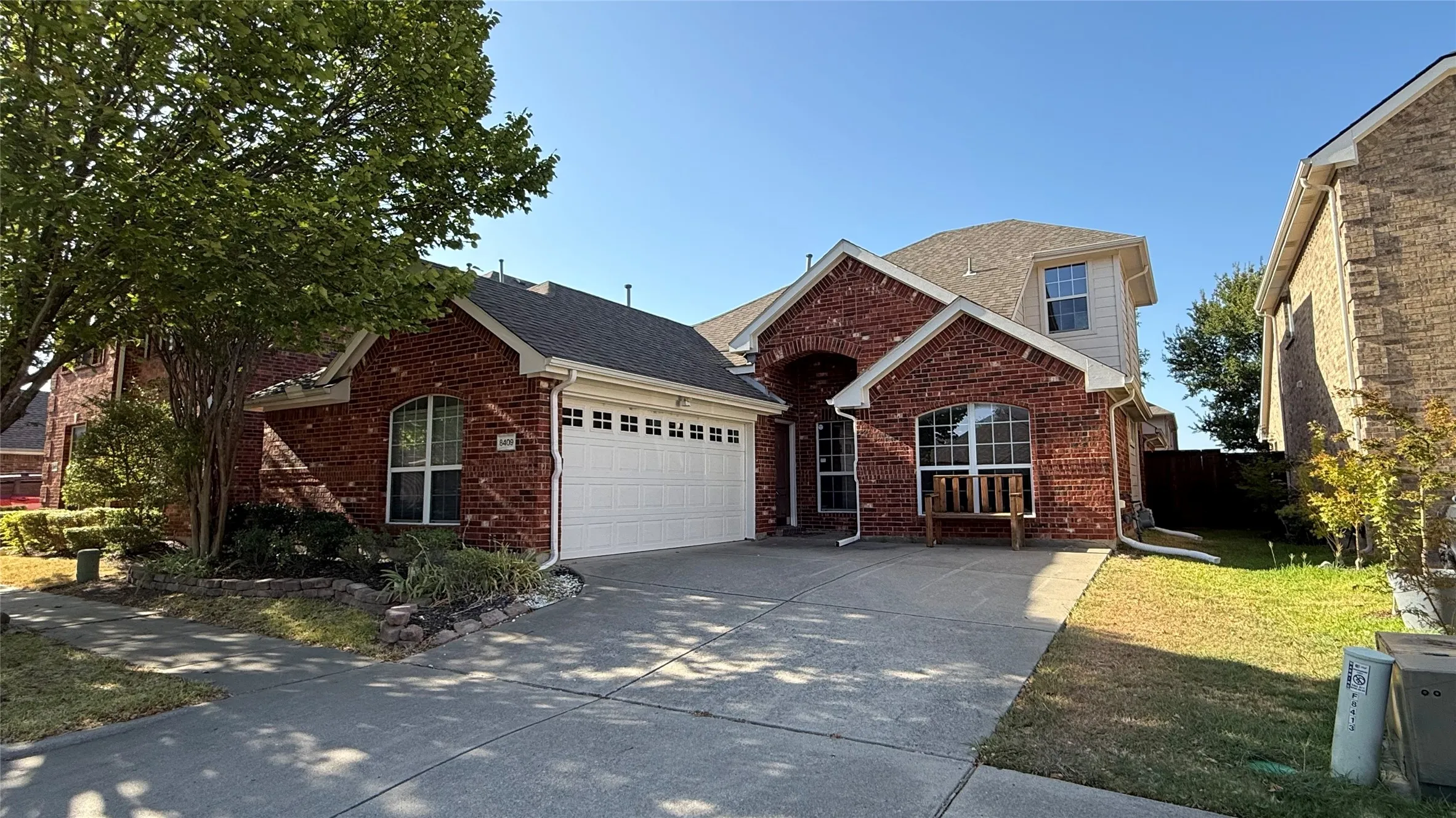 Brick exterior with a two-car garage, concrete driveway, and established landscaping