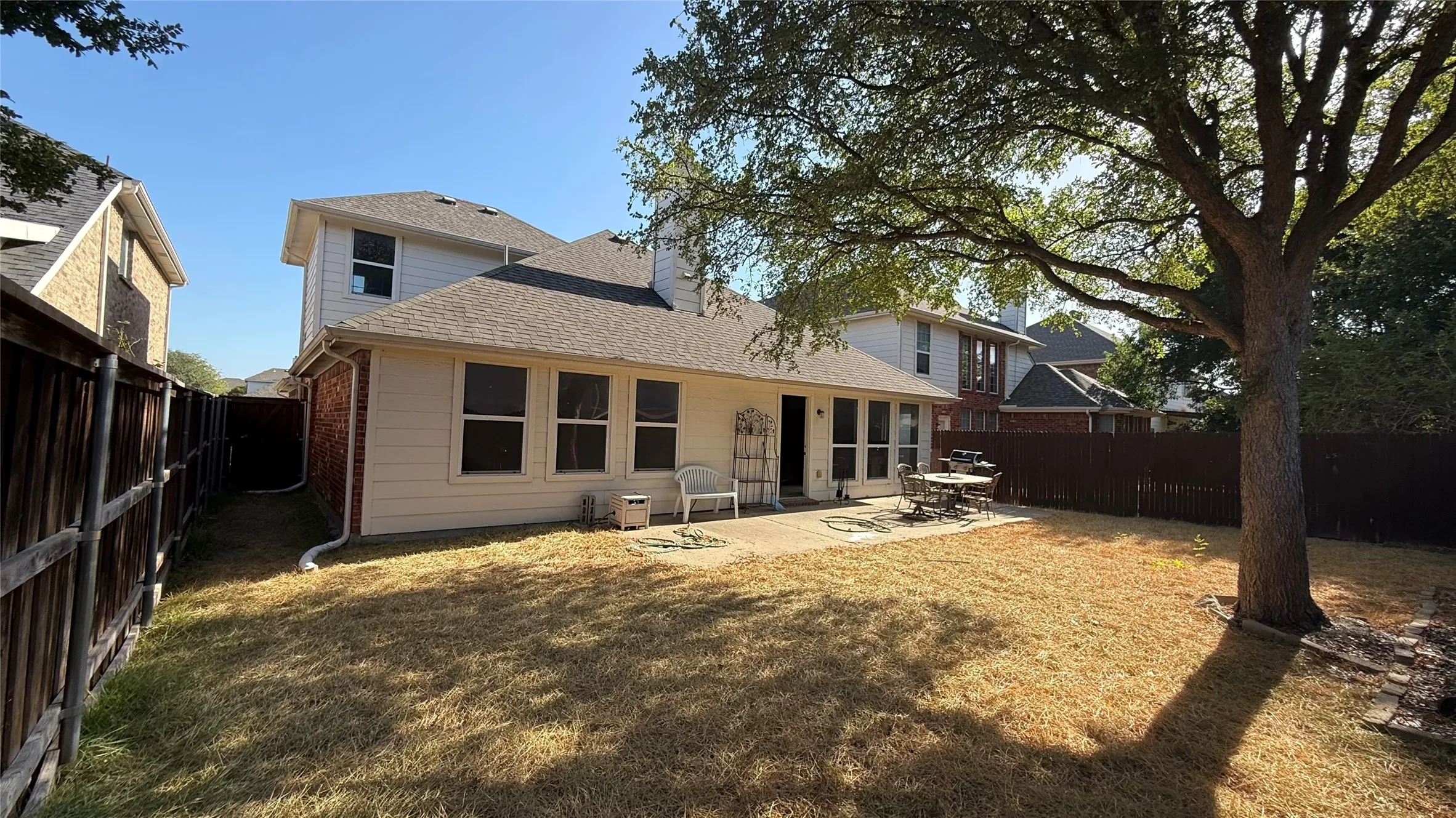 Expansive fenced backyard featuring a concrete patio, mature tree, and exterior siding