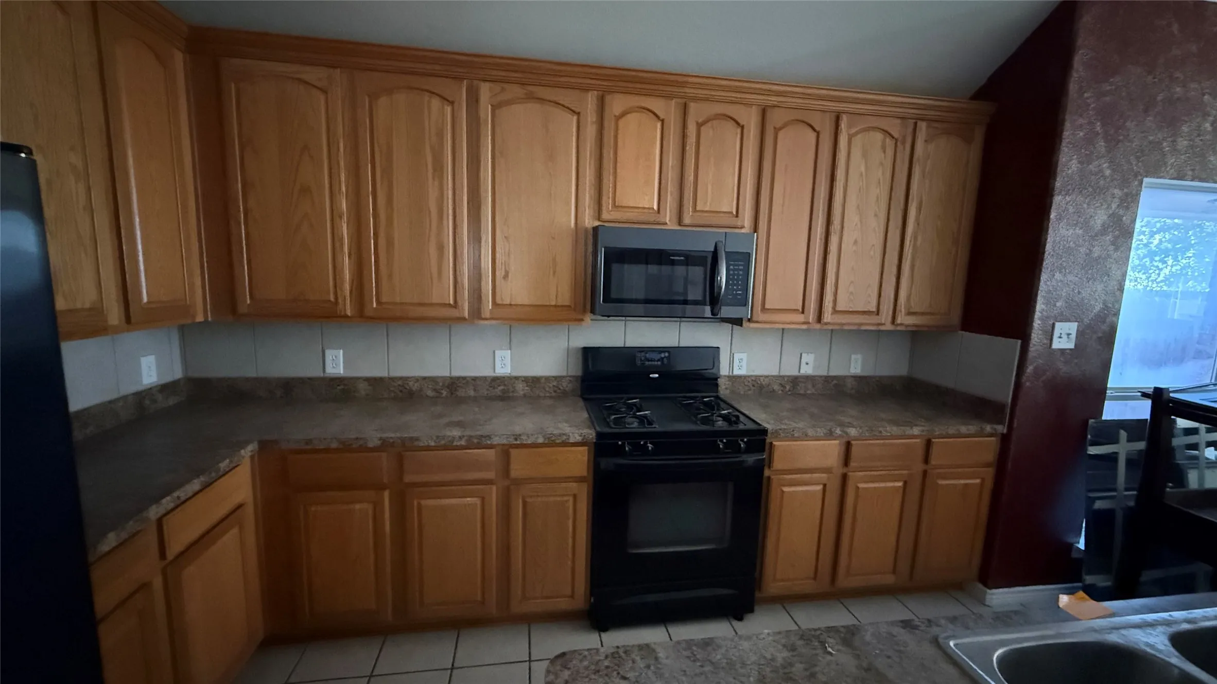 Wood-finish cabinetry with dark hardware, a black range, and a coordinating built-in microwave