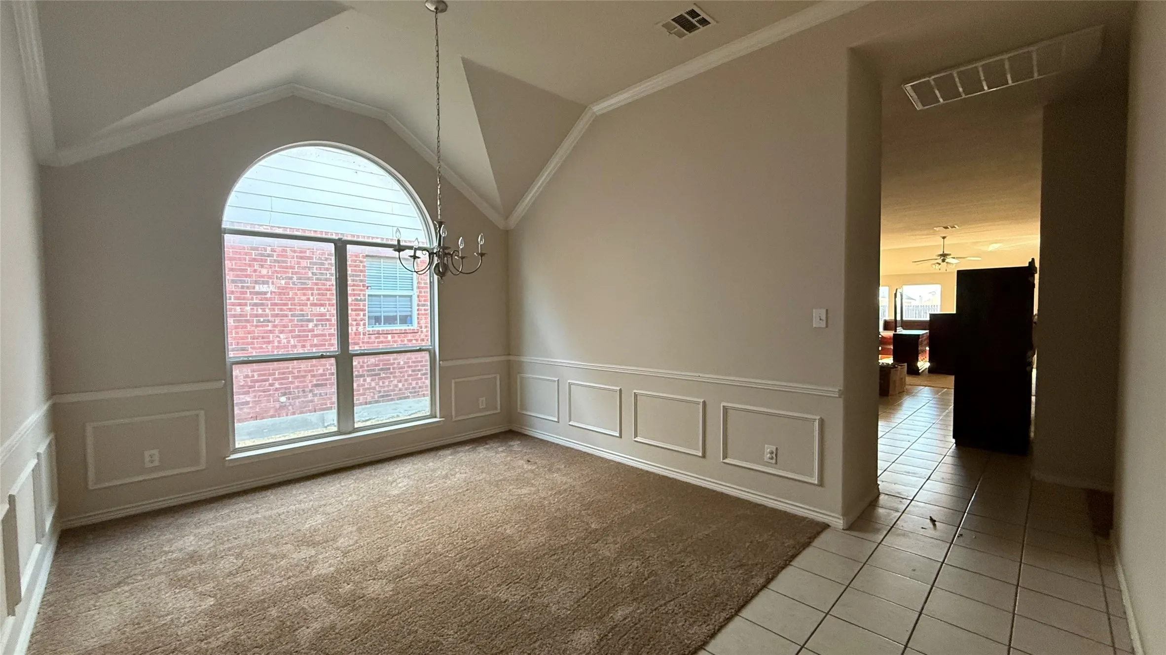 Vaulted ceiling with crown molding, decorative wainscoting, arched window, chandelier, and mixed flooring