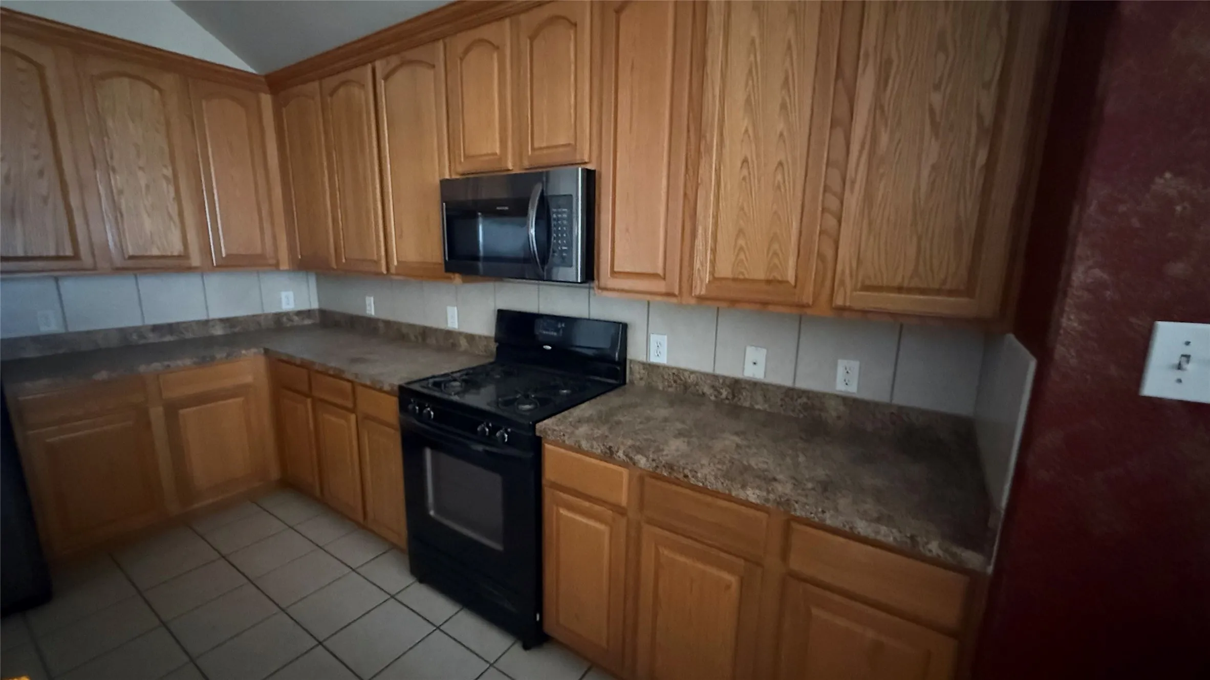 Wood-finish cabinetry, tile flooring, stainless steel microwave, black electric range, and laminate countertops