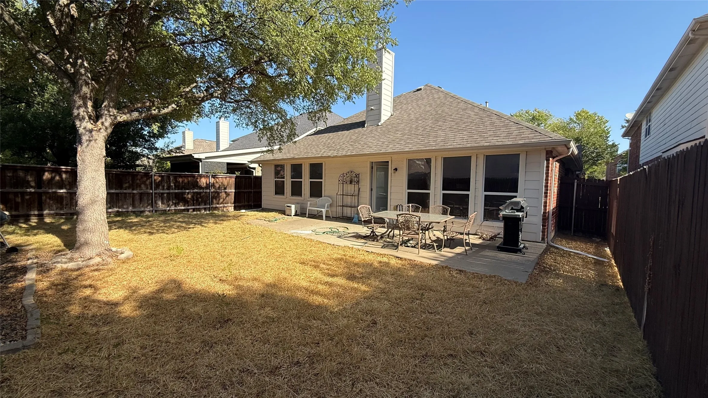 Spacious backyard featuring a mature tree, concrete patio, and privacy fencing