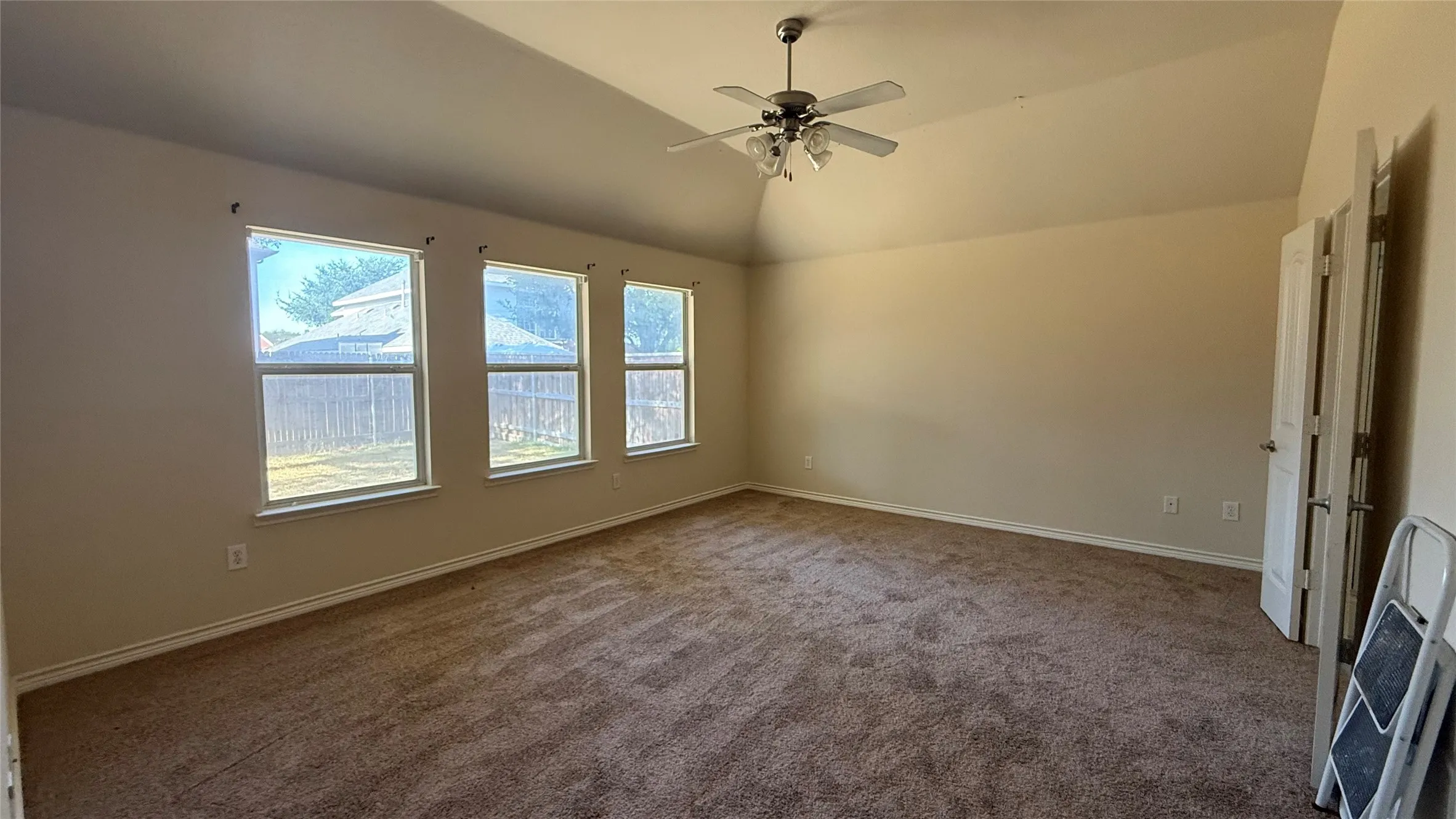 Vaulted ceiling with an attached ceiling fan, three windows, and carpet flooring
