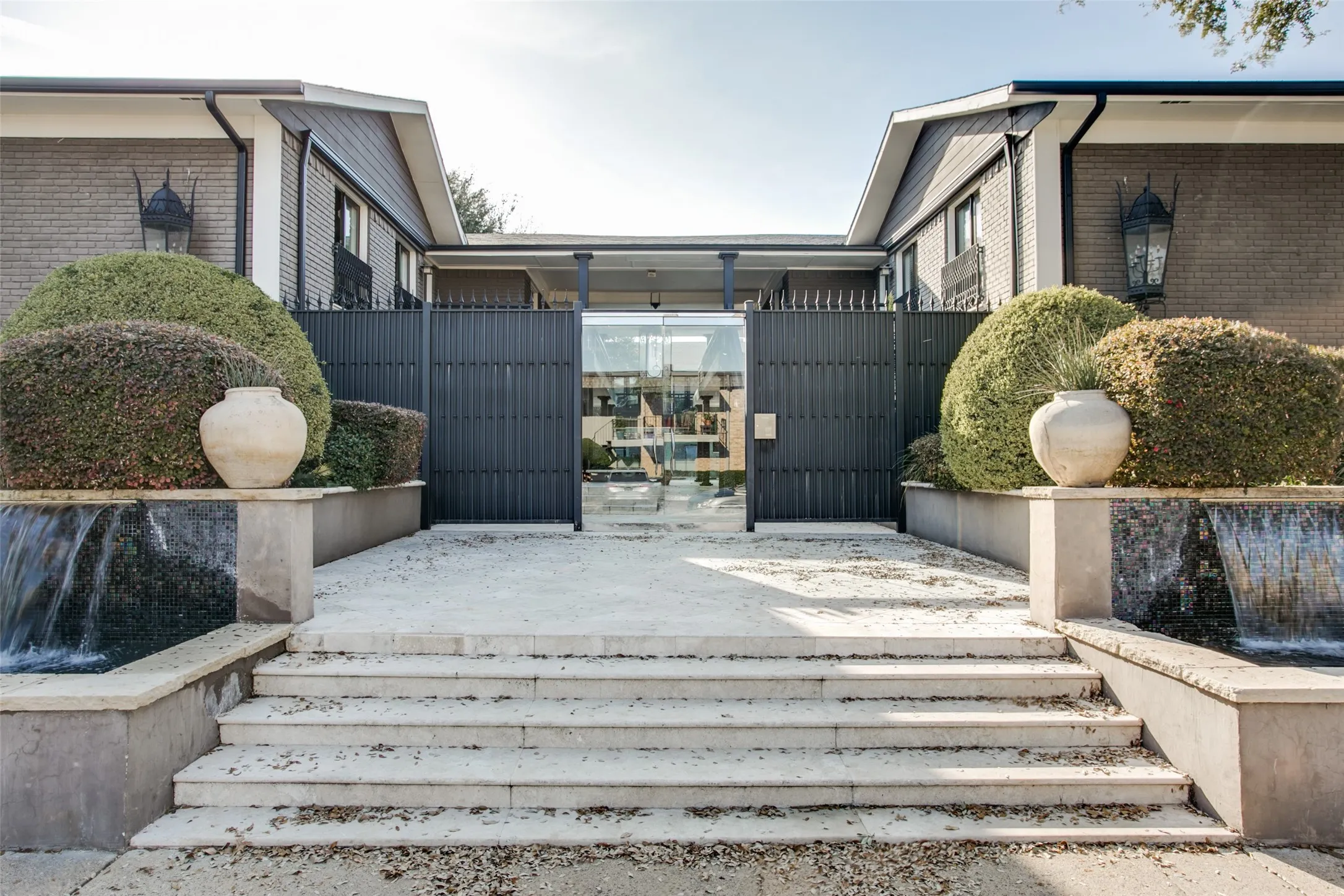 Stone staircase leading to an entry courtyard with water features, landscaping, and a privacy gate