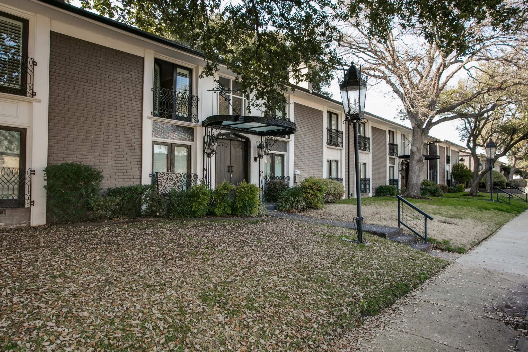 Exterior with brick and stucco facade, decorative ironwork balconies, and mature trees lining the property