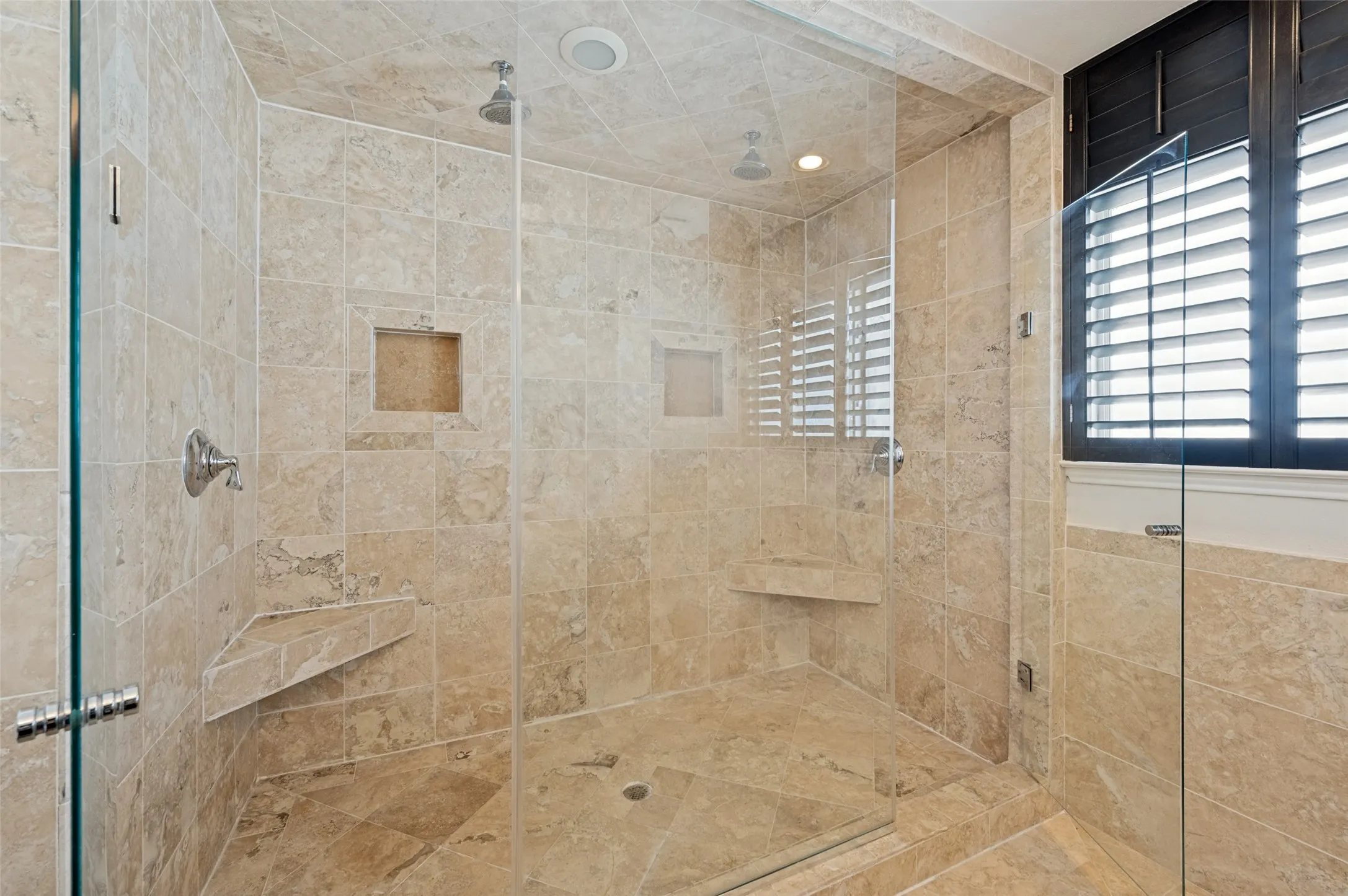Glass-enclosed shower featuring natural stone tiling, a built-in shower bench, recessed wall niche, and a rain shower head