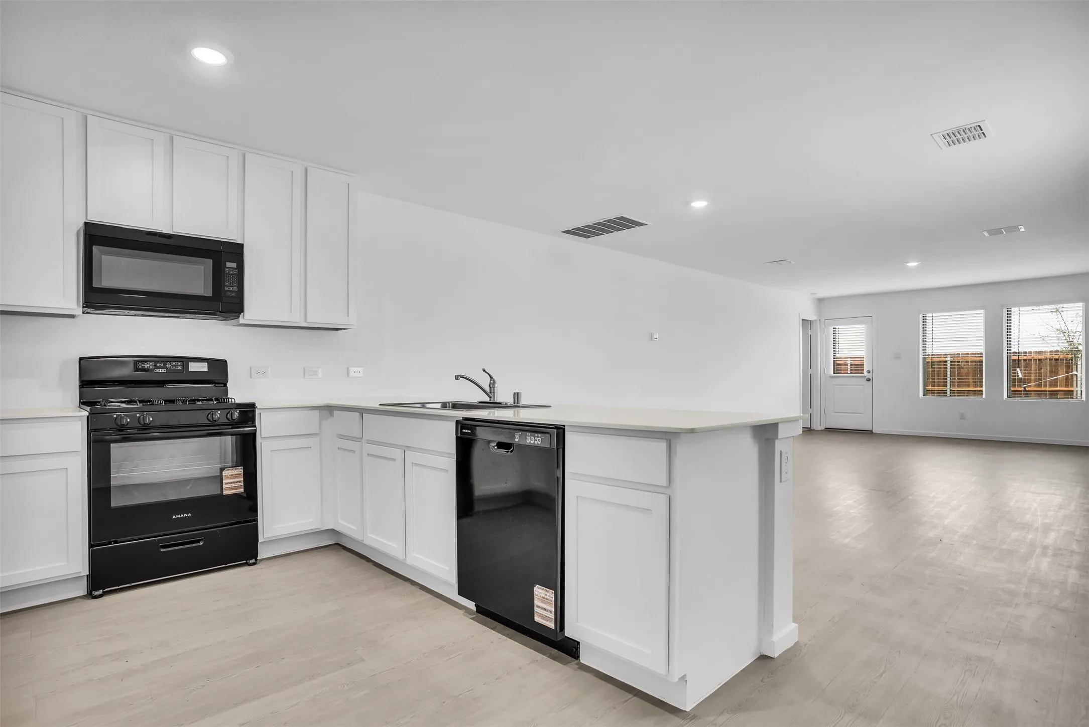 Kitchen with black appliances, recessed lighting, a peninsula, white cabinetry, and light wood-type flooring