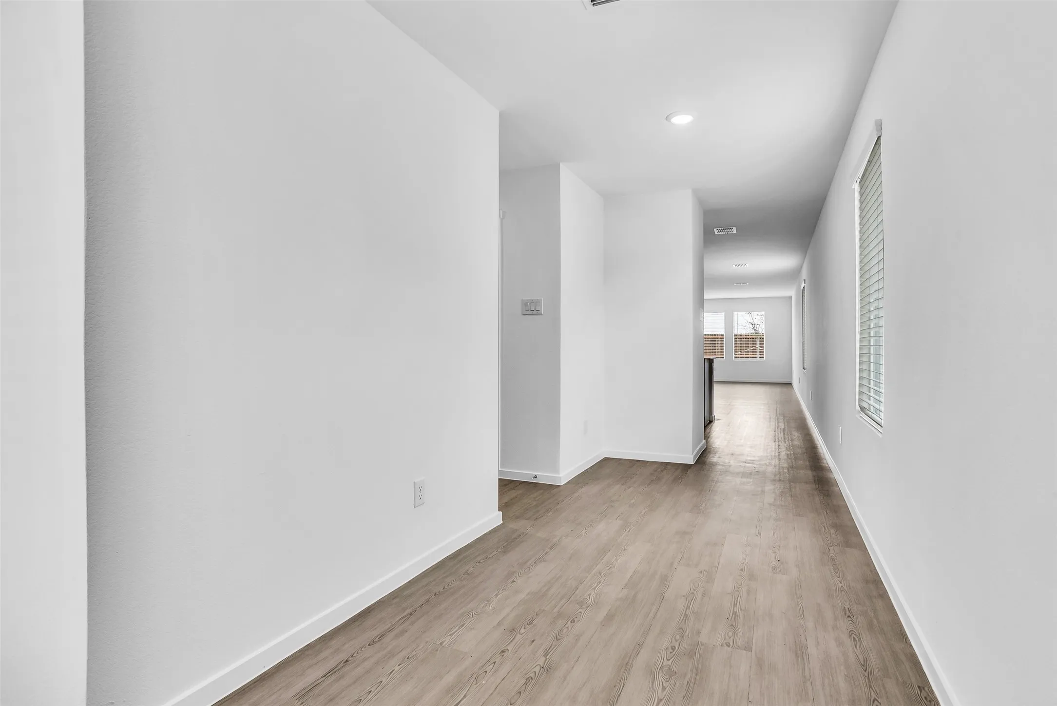 Hallway with light wood-style floors and recessed lighting
