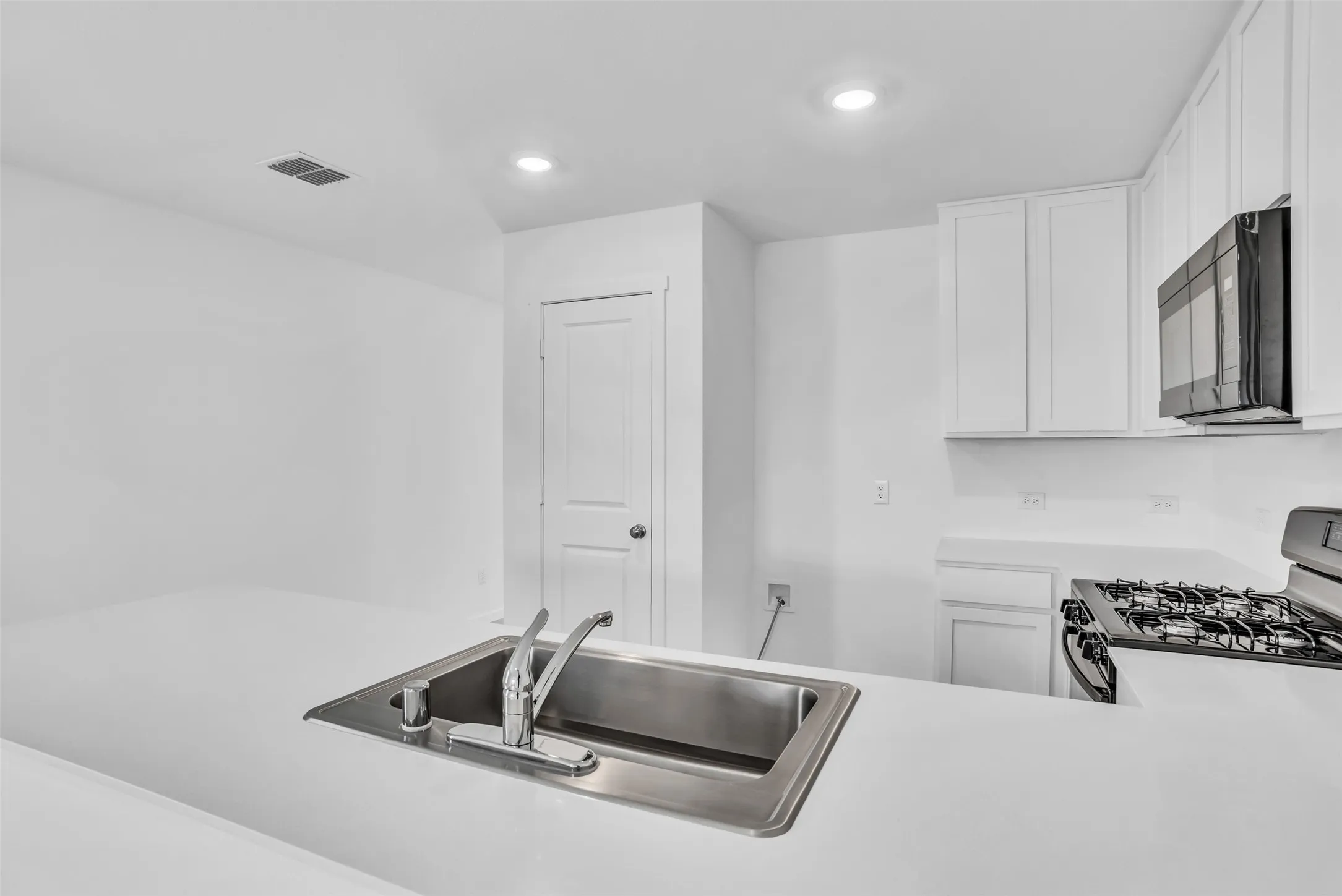 Kitchen featuring light countertops, range with gas cooktop, white cabinets, black microwave, and recessed lighting