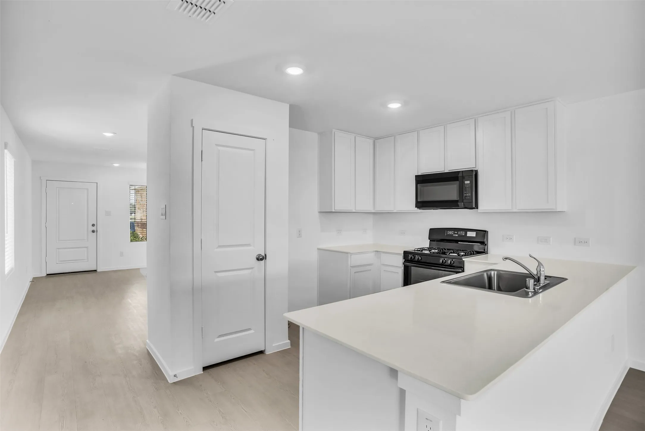 Kitchen with black appliances, white cabinets, a peninsula, light wood-style floors, and recessed lighting