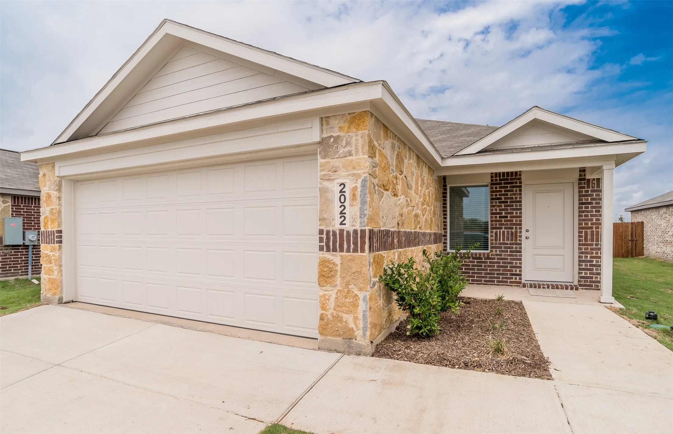Ranch-style home featuring brick siding, stone siding, driveway, an attached garage, and covered porch