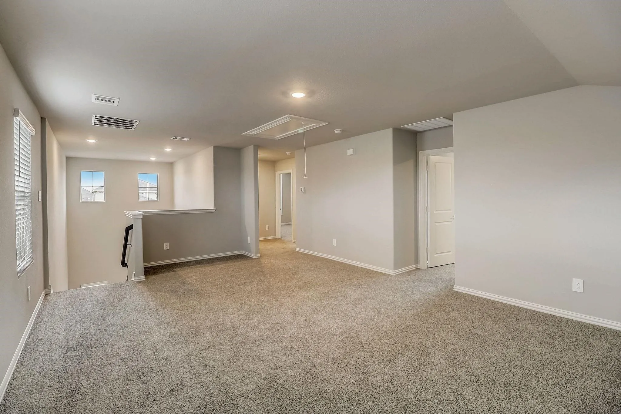 Expansive carpeted area with recessed lighting, multiple windows with blinds, a white balustrade, and a white interior door