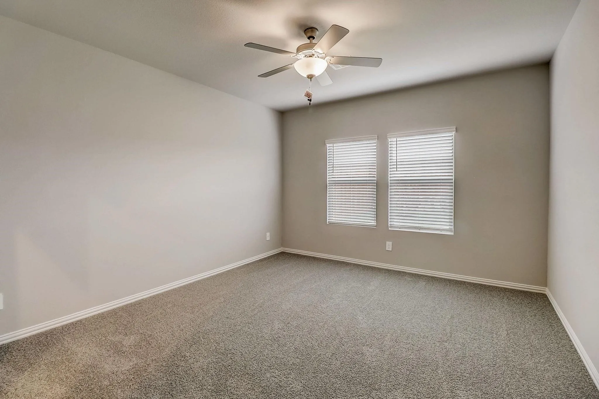 Vaulted ceiling, two windows with horizontal blinds, ceiling fan with integrated lighting, neutral wall paint, and gray carpeting