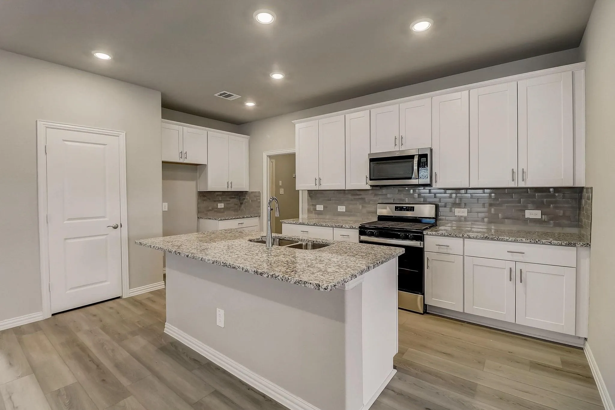 Kitchen featuring an island with a dual-basin sink, overhead recessed lighting, granite countertops, wood-finish flooring, and white cabinetry