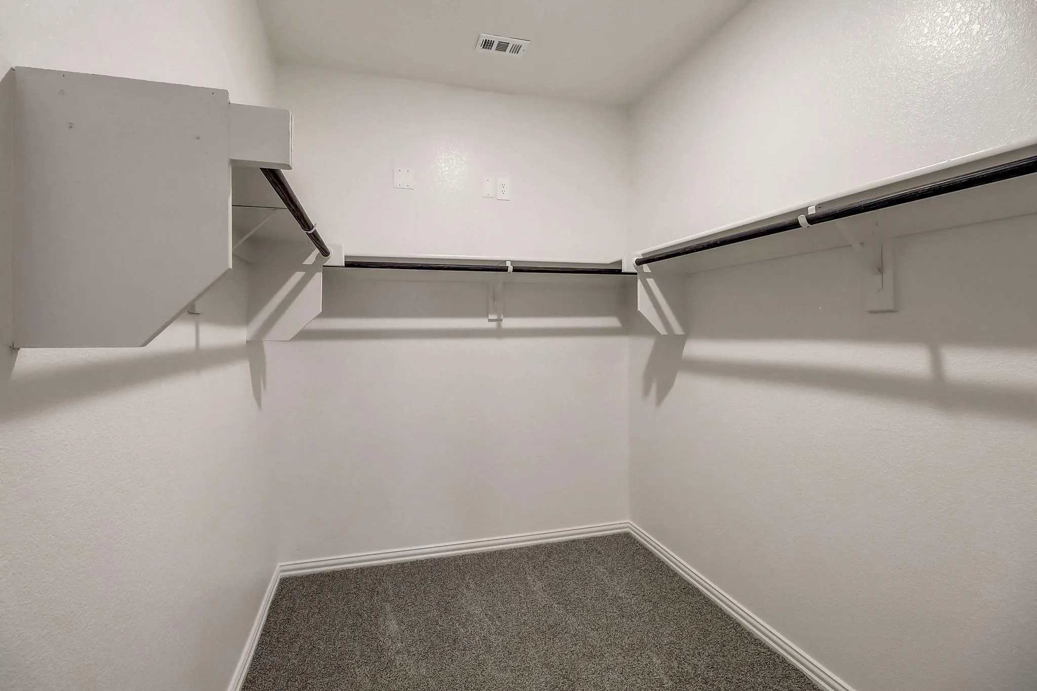 Walk-in closet featuring white built-in shelving, hanging rods, and gray carpet flooring