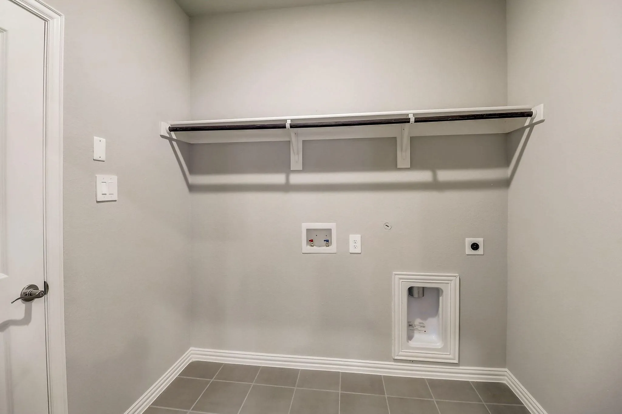 Utility room featuring a built-in shelf with a hanging rod, tile flooring, and light-toned walls