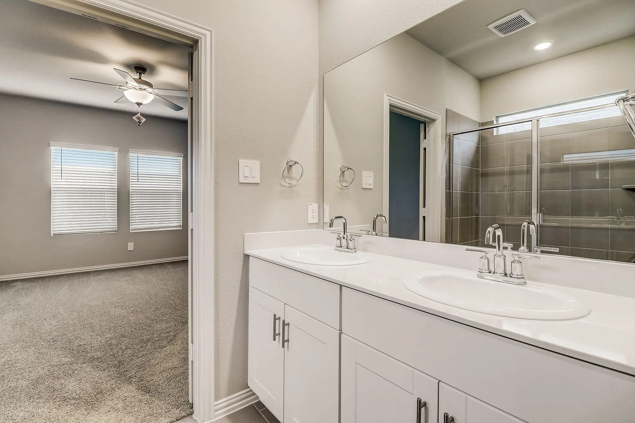 Dual vanity with white countertops, chrome fixtures, and a glass-enclosed shower featuring tiled walls