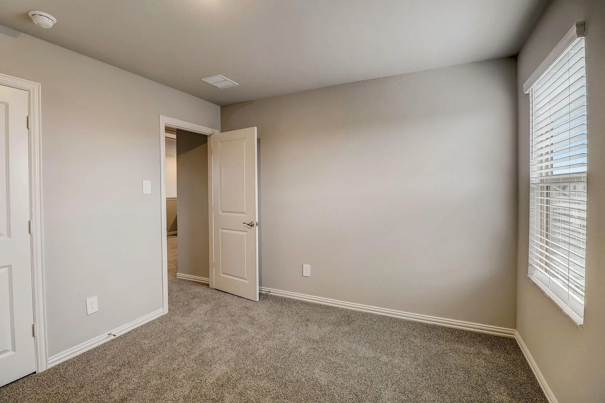 Neutral tone walls, textured carpeting, panel doors with brushed nickel hardware, and a window with blinds