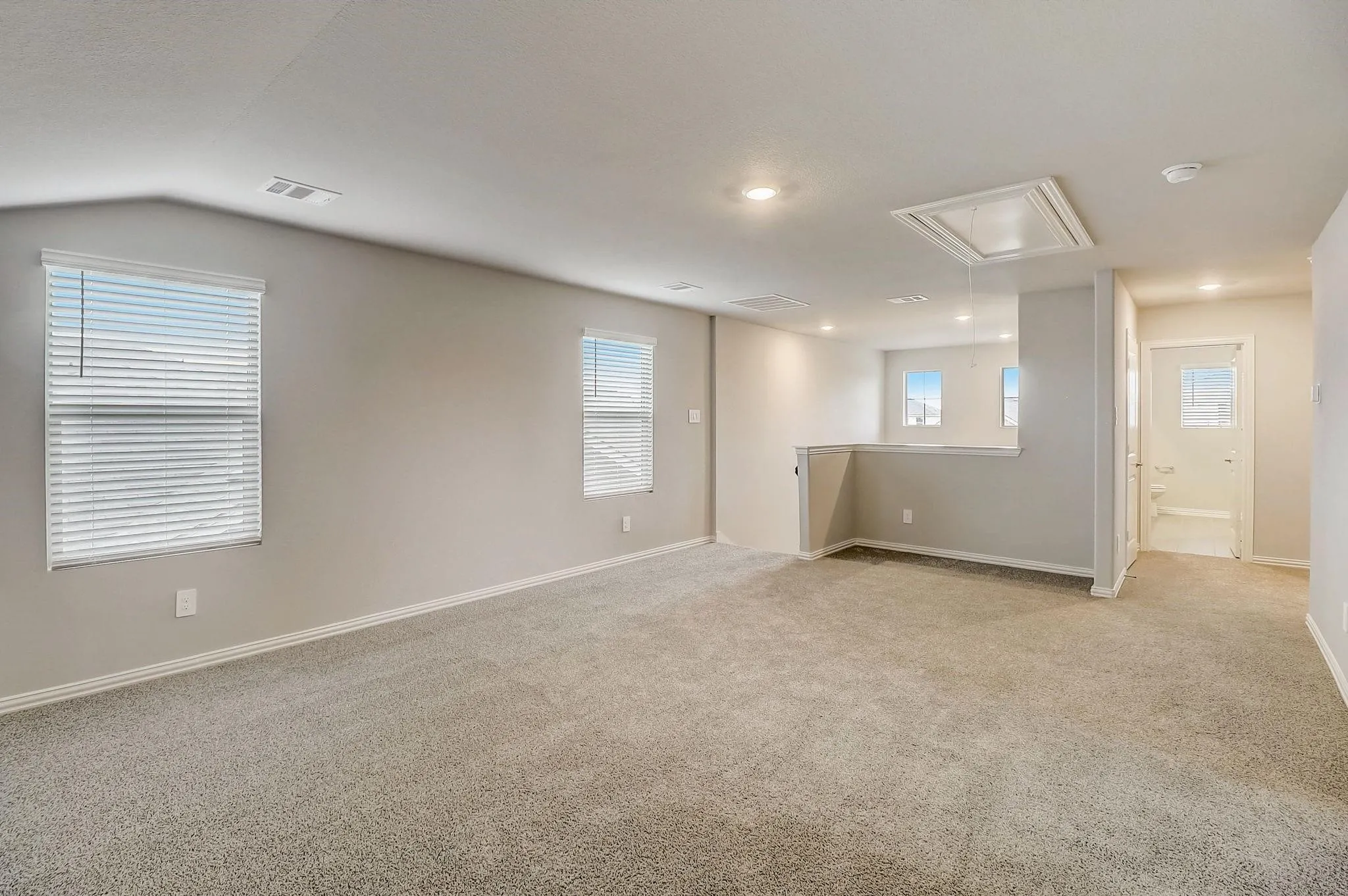 Spacious carpeted room featuring multiple windows with blinds, recessed lighting, and access to a separate area