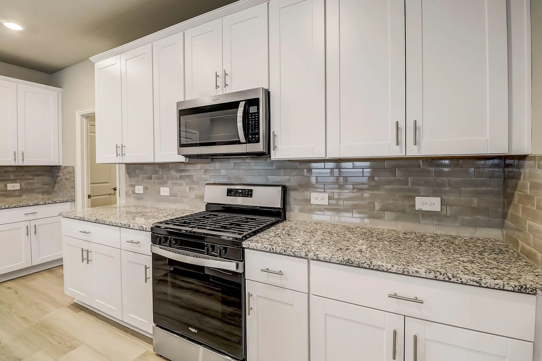 White shaker-style cabinetry, granite countertops, tile backsplash, stainless steel appliances, and wood-finish flooring