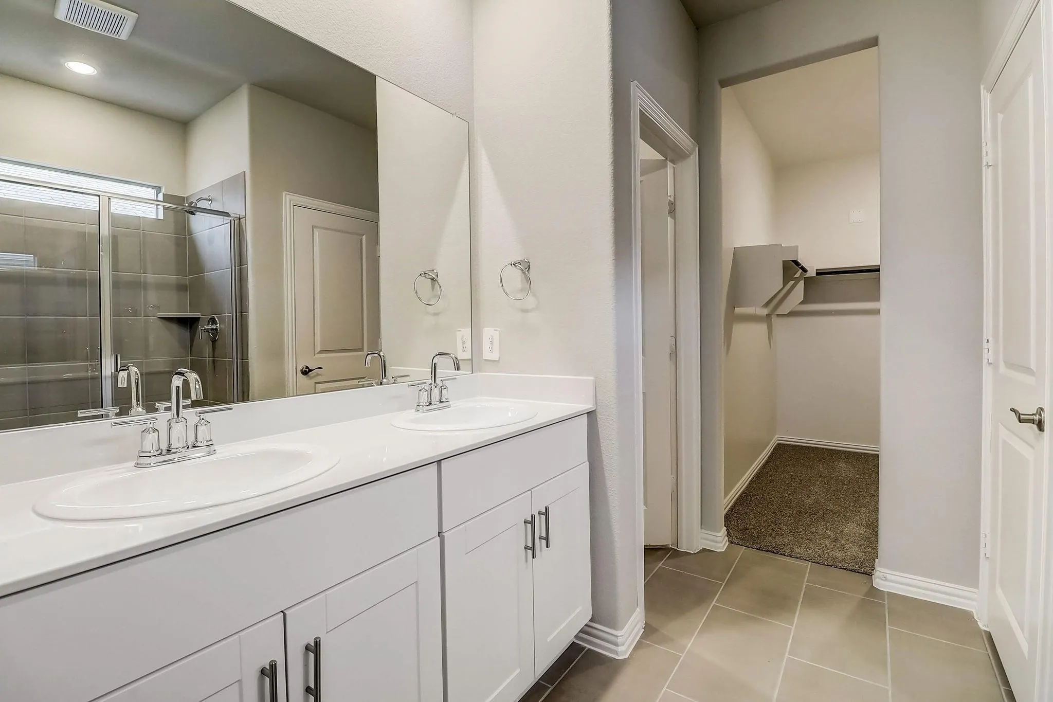 Dual vanity with white cabinetry, polished chrome fixtures, and a spacious walk-in closet