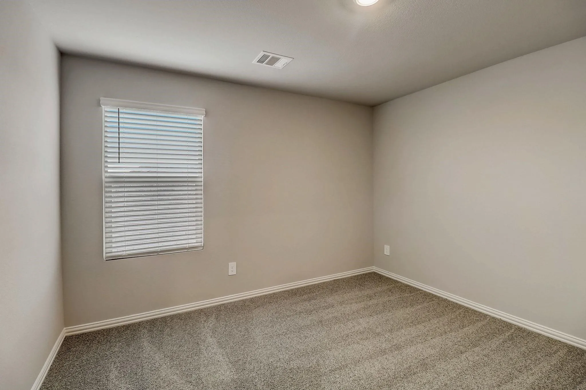 Neutral-toned carpeting, light-colored walls, and a window with blinds