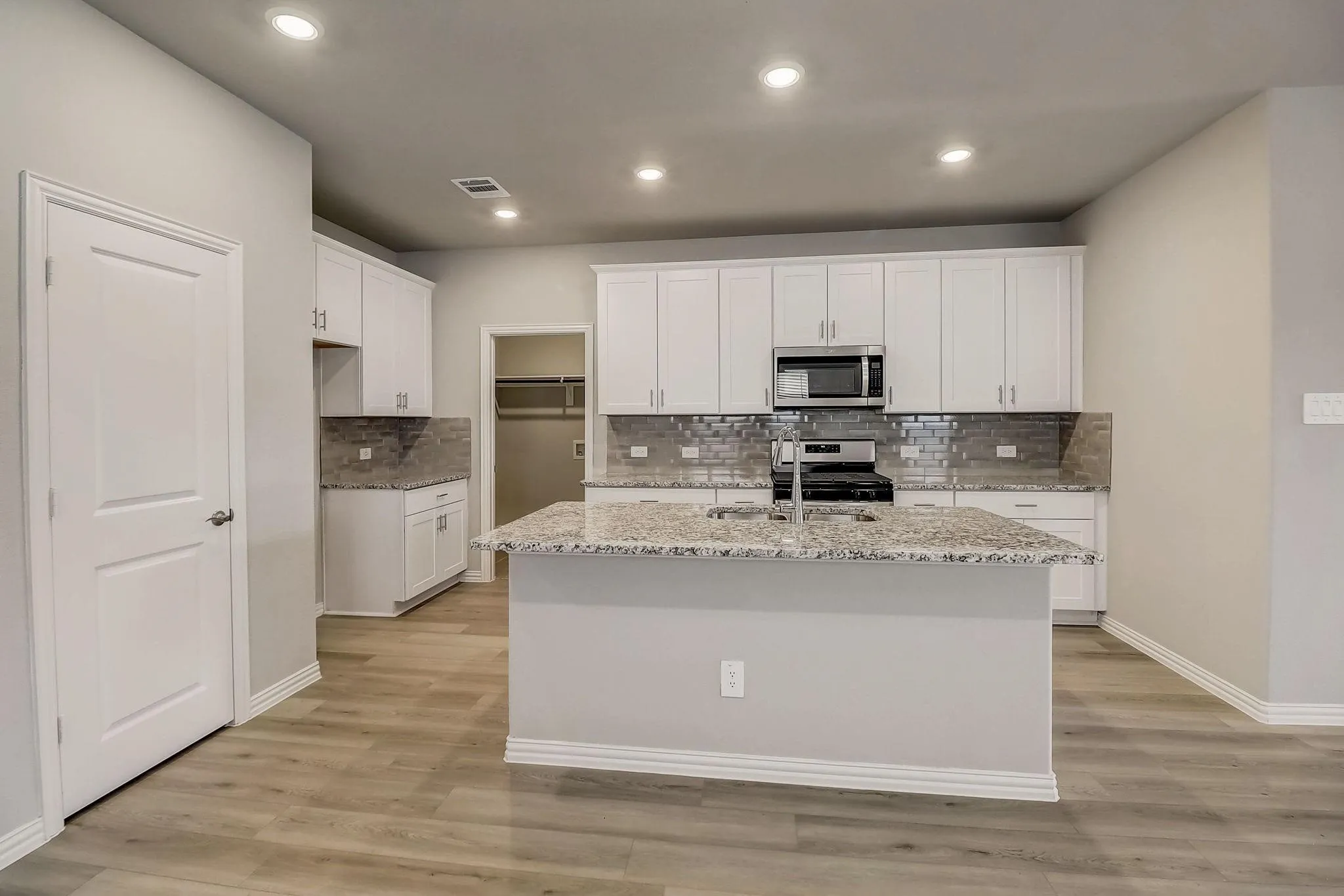 Kitchen featuring an island with a sink, white cabinetry, integrated stainless steel appliances, a tile backsplash, and wood-finish flooring