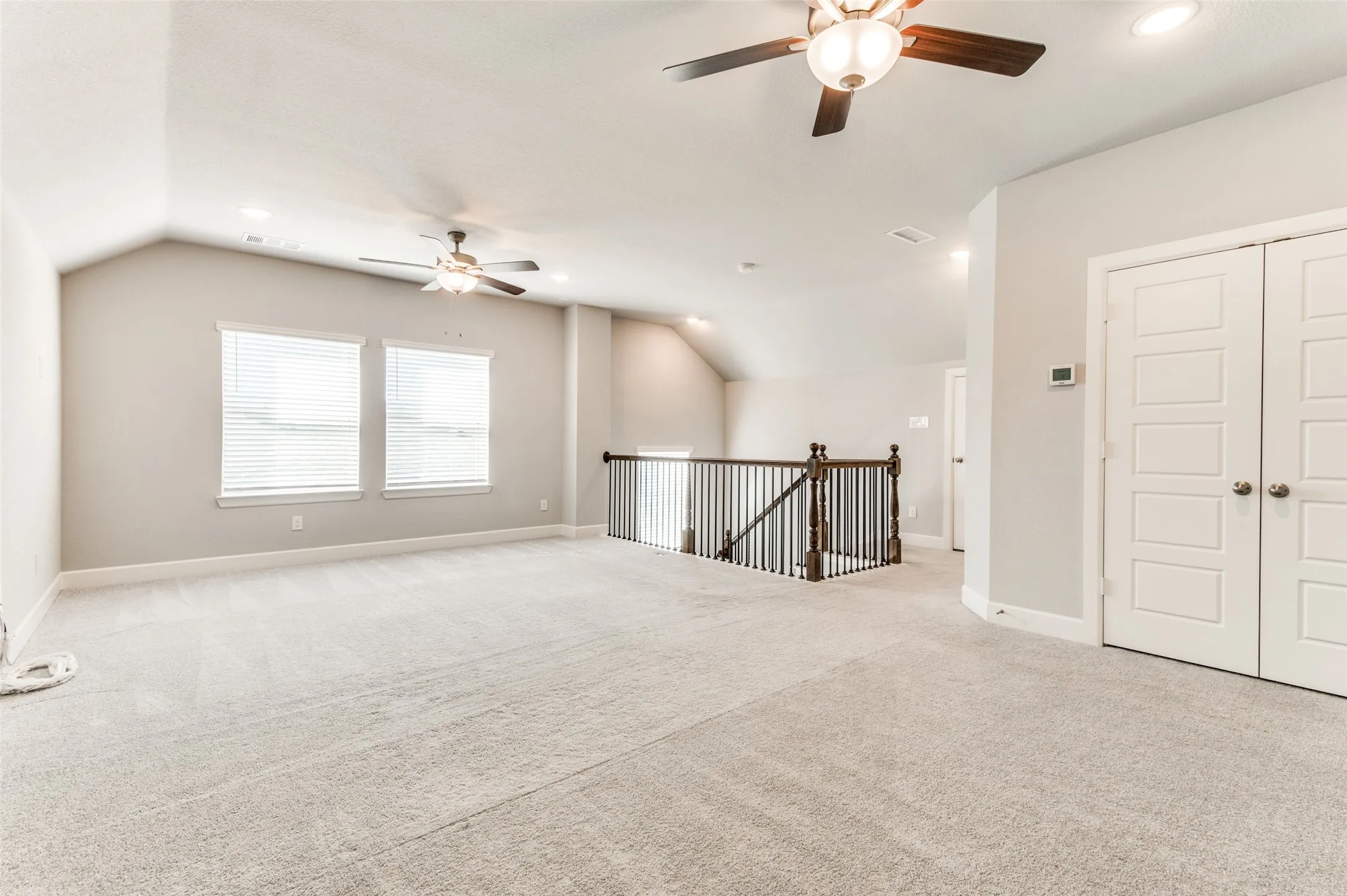 Spacious carpeted area with vaulted ceilings, multiple windows with blinds, and recessed lighting